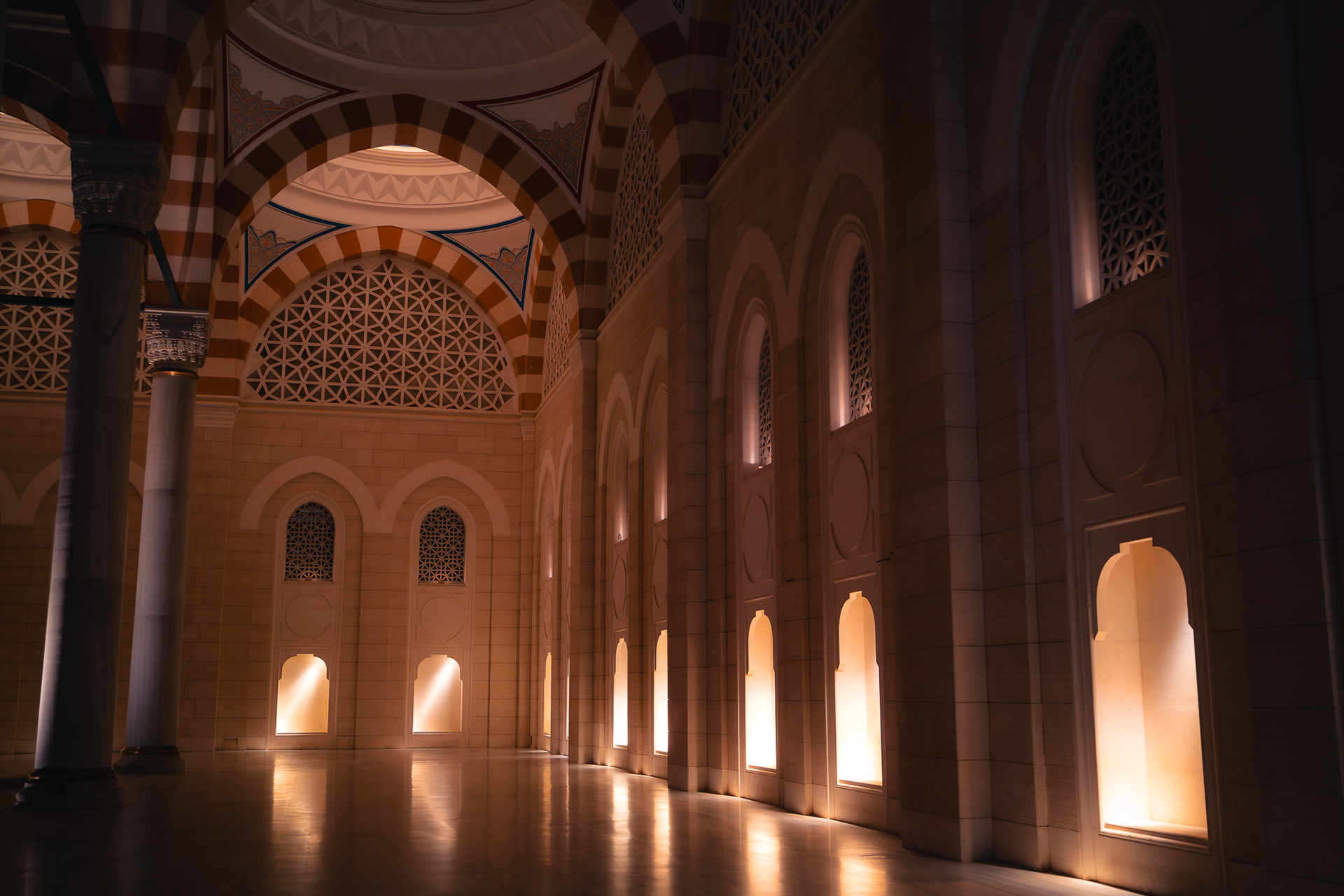 Détail architectural d'une mosquée par Sabri Kaced, illustrant des arches décorées et des niches lumineuses créant un jeu d'ombres et de reflets sur le sol en marbre.