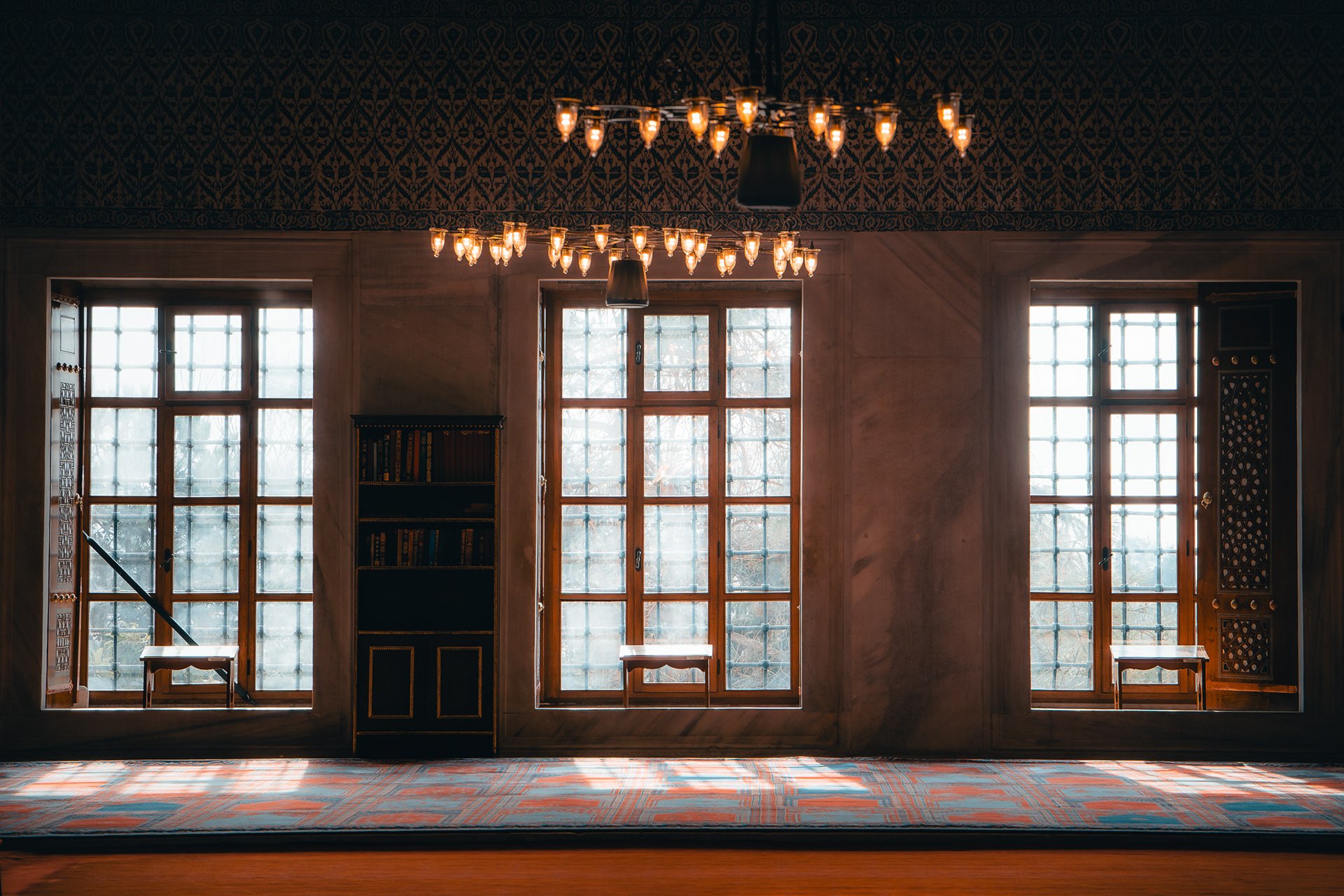 Vue intérieure minimaliste par Sabri Kaced montrant trois fenêtres lumineuses et des lustres bas dans une salle de prière à Istanbul.