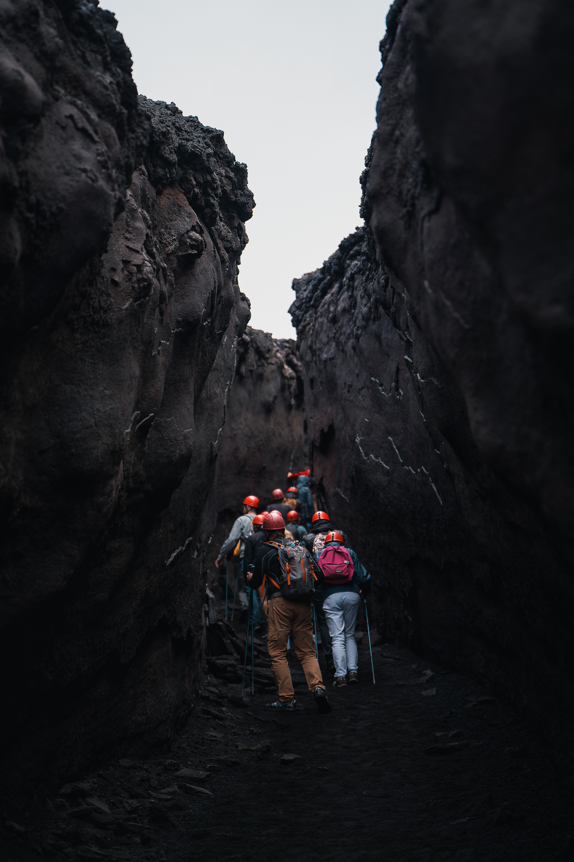 Groupe de randonneurs équipés de casques rouges et de bâtons de marche explorant une étroite crevasse de lave refroidie sur un volcan.