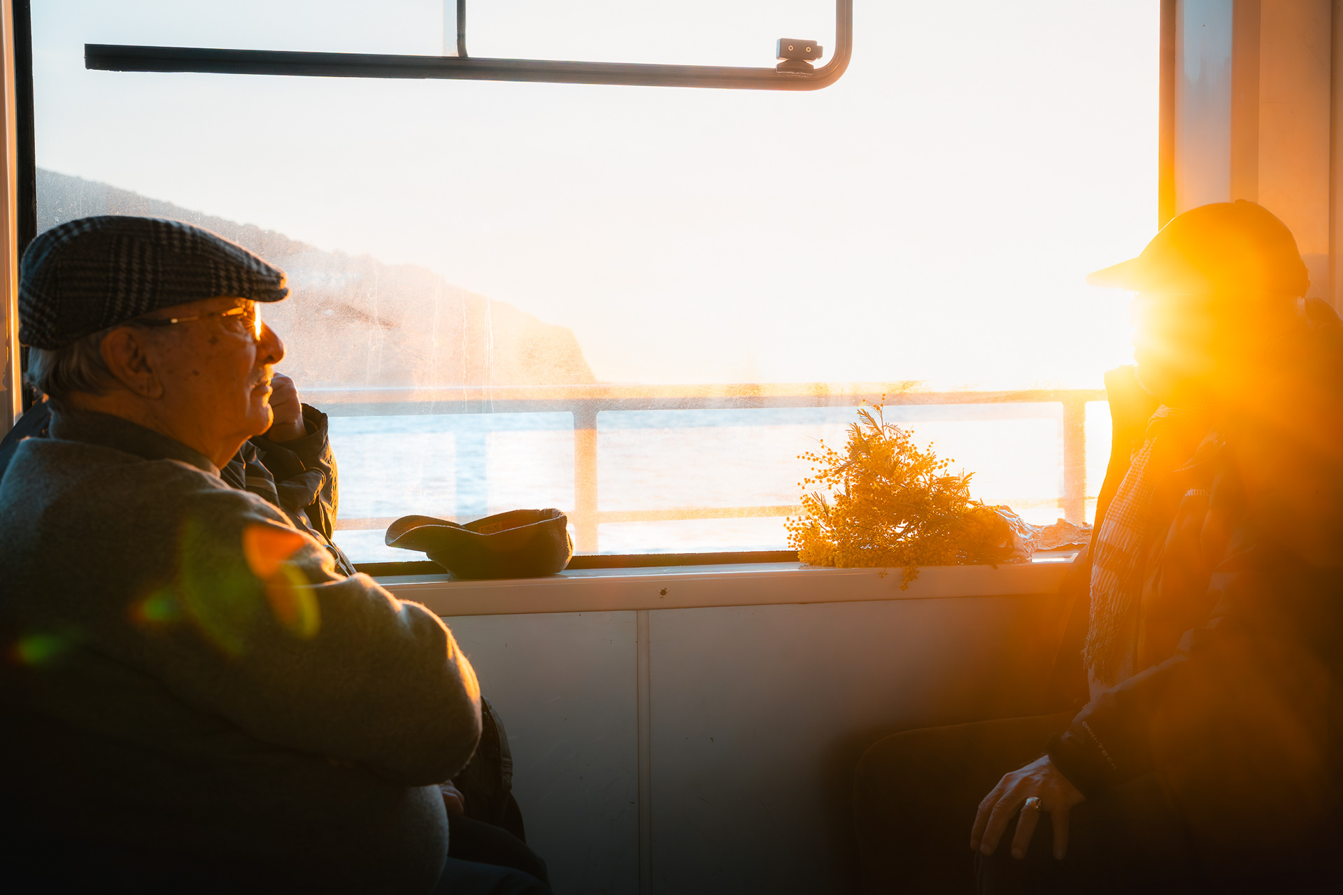 Photo documentaire par Sabri Kaced de deux hommes discutant sur un ferry, baignés dans une lumière dorée intense de contre-jour.