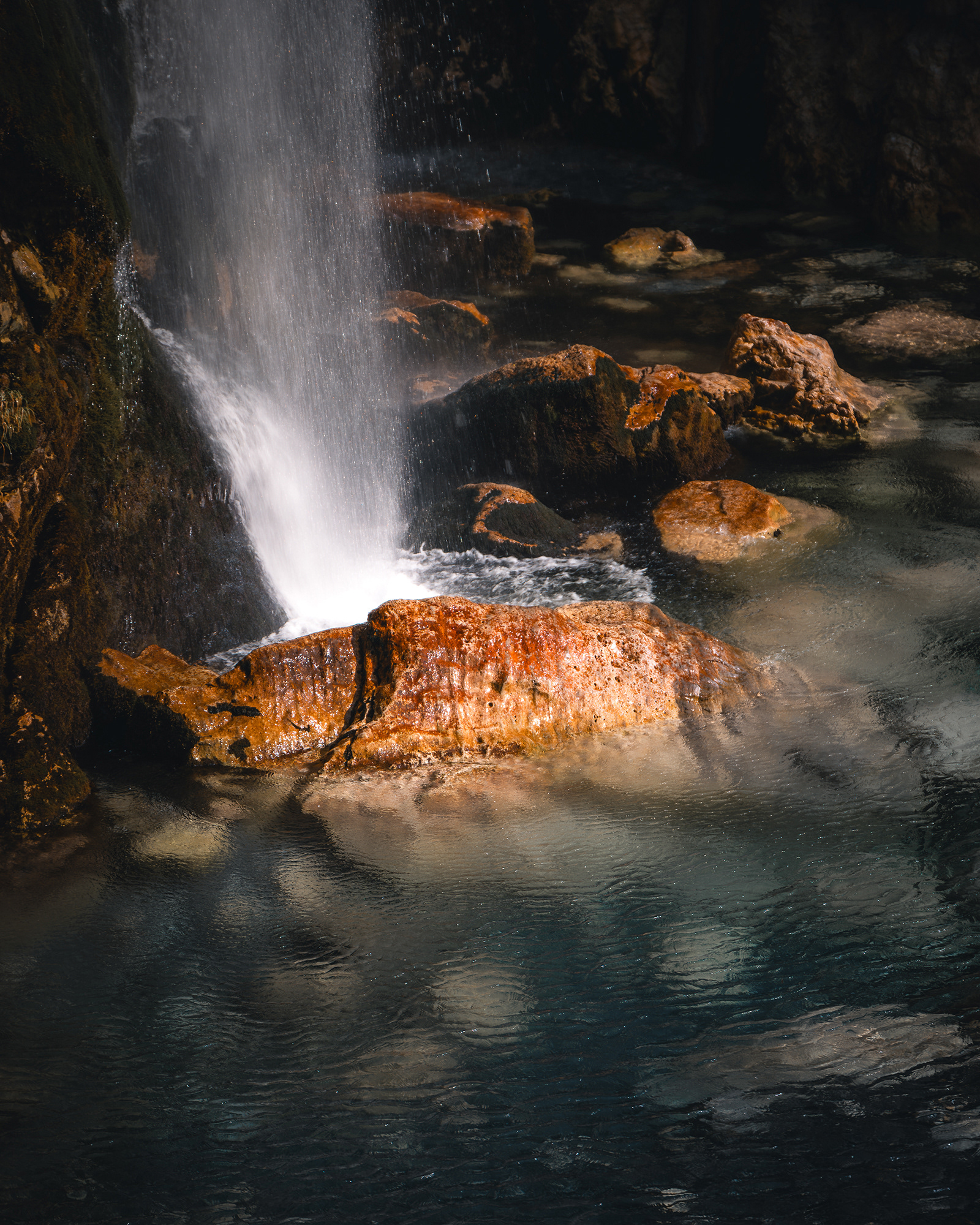 Gros plan artistique sur l'eau d'une cascade frappant des rochers aux teintes ocres, capturant la texture et le mouvement de l'eau. Photo : Sabri Kaced.