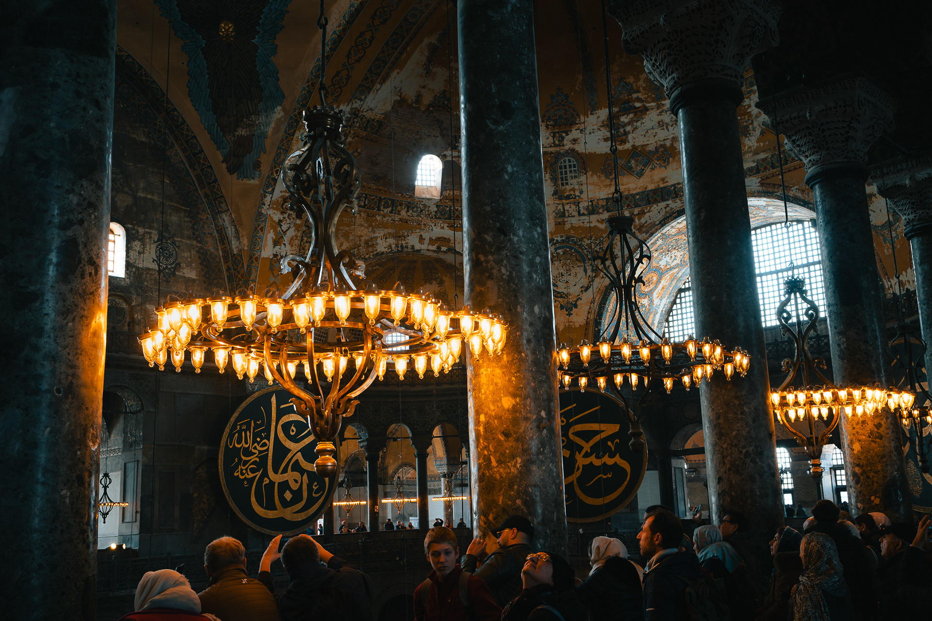 Ambiance intérieure de Sainte-Sophie montrant les lustres circulaires dorés et les colonnes de marbre, par Sabri Kaced.
