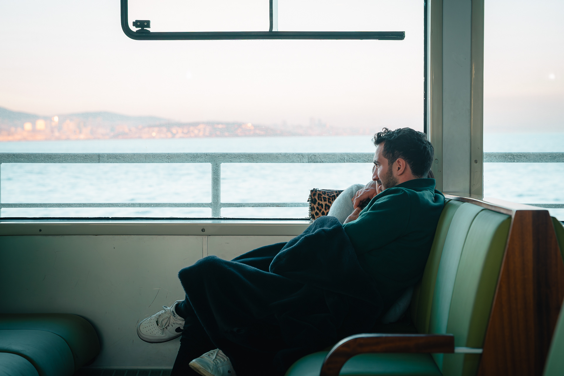 Photographie de Sabri Kaced montrant un homme de profil assis dans un ferry, contemplant la mer à travers la vitre au lever du soleil.