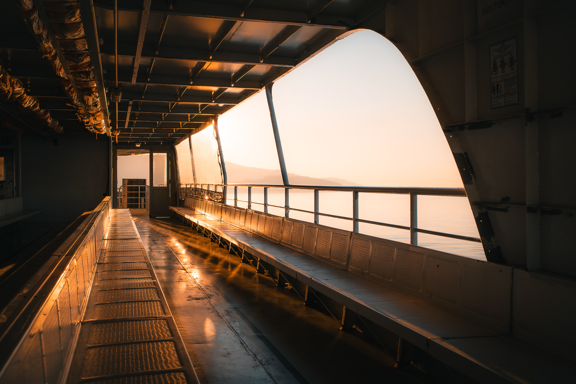 Vue architecturale du pont intérieur d'un ferry vide, capturée par Sabri Kaced, mettant en avant les lignes de fuite et les reflets du soleil au sol.
