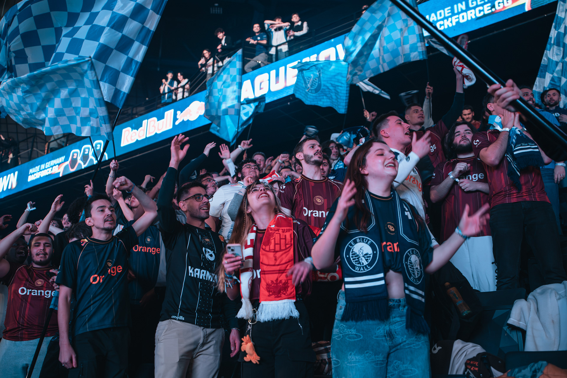 Foule de supporters de la Karmine Corp en liesse dans les tribunes, agitant des drapeaux à damier bleu et blanc lors d'un événement d'esport.