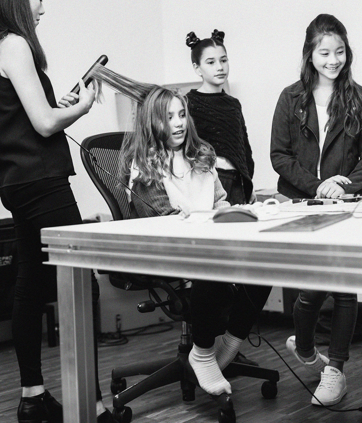 Production for Disney Channel. Another scene photo in black and white of the make up process. Make up artist is working with the hair of one young lady, few other around smiling. A film by Emotion Graphics. Cast for TV Xmans IDS in Munich. Video Production and film Animation GErmany. Photo by Rob Adalierd - Aitor Benavent, Executive Director.