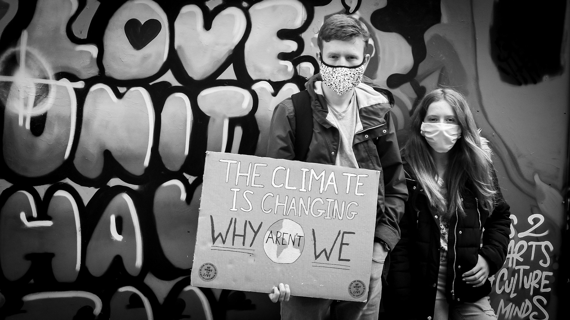 Two teenagers holding a cardboard sign with the words "The Climate is Changing Why Aren't We" written on it.