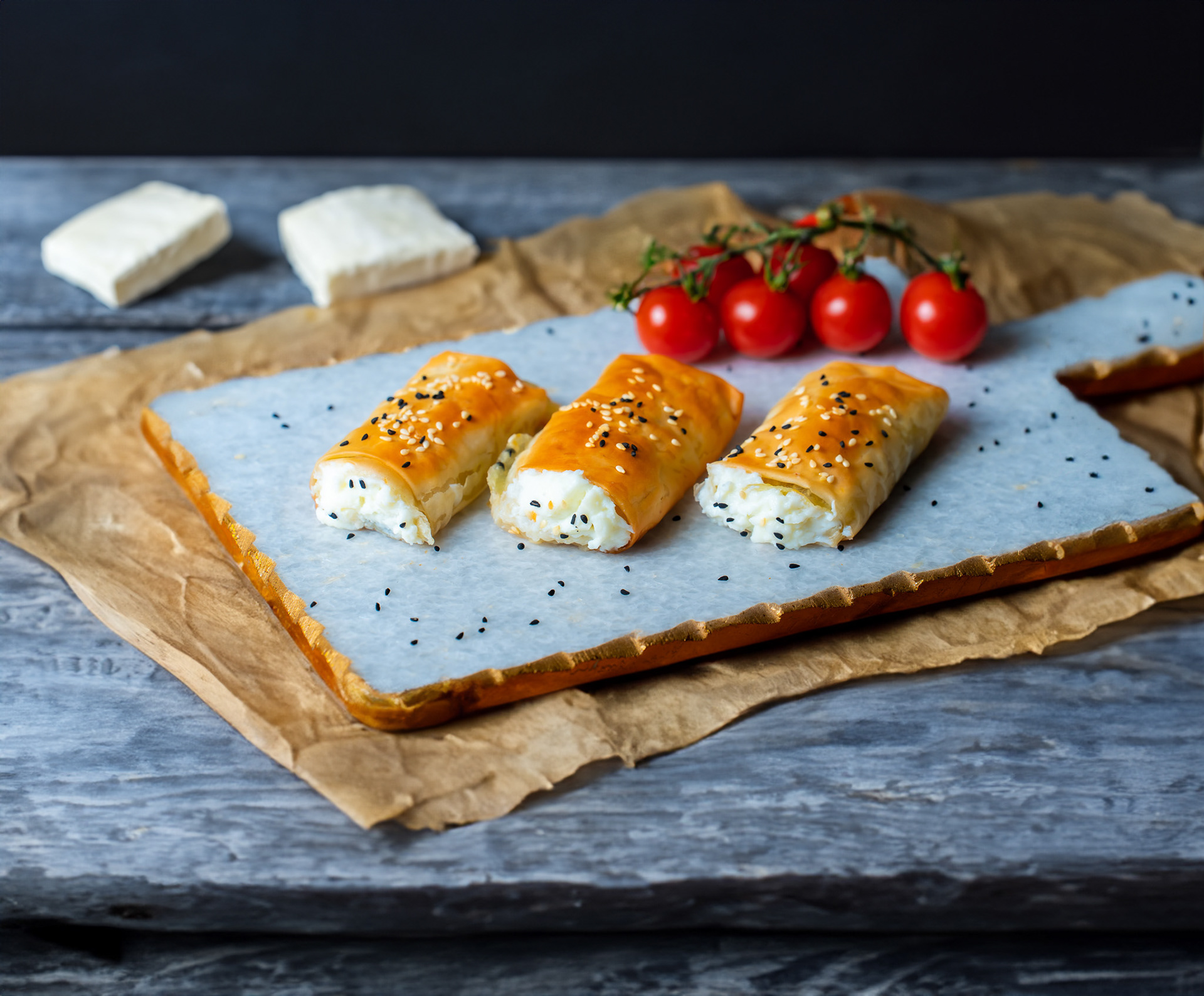 Golden crispy cheese pastries on a rustic board with fresh cherry tomatoes, professional bakery and breakfast photography for Toronto cafes, catering menus, and artisanal food marketing.