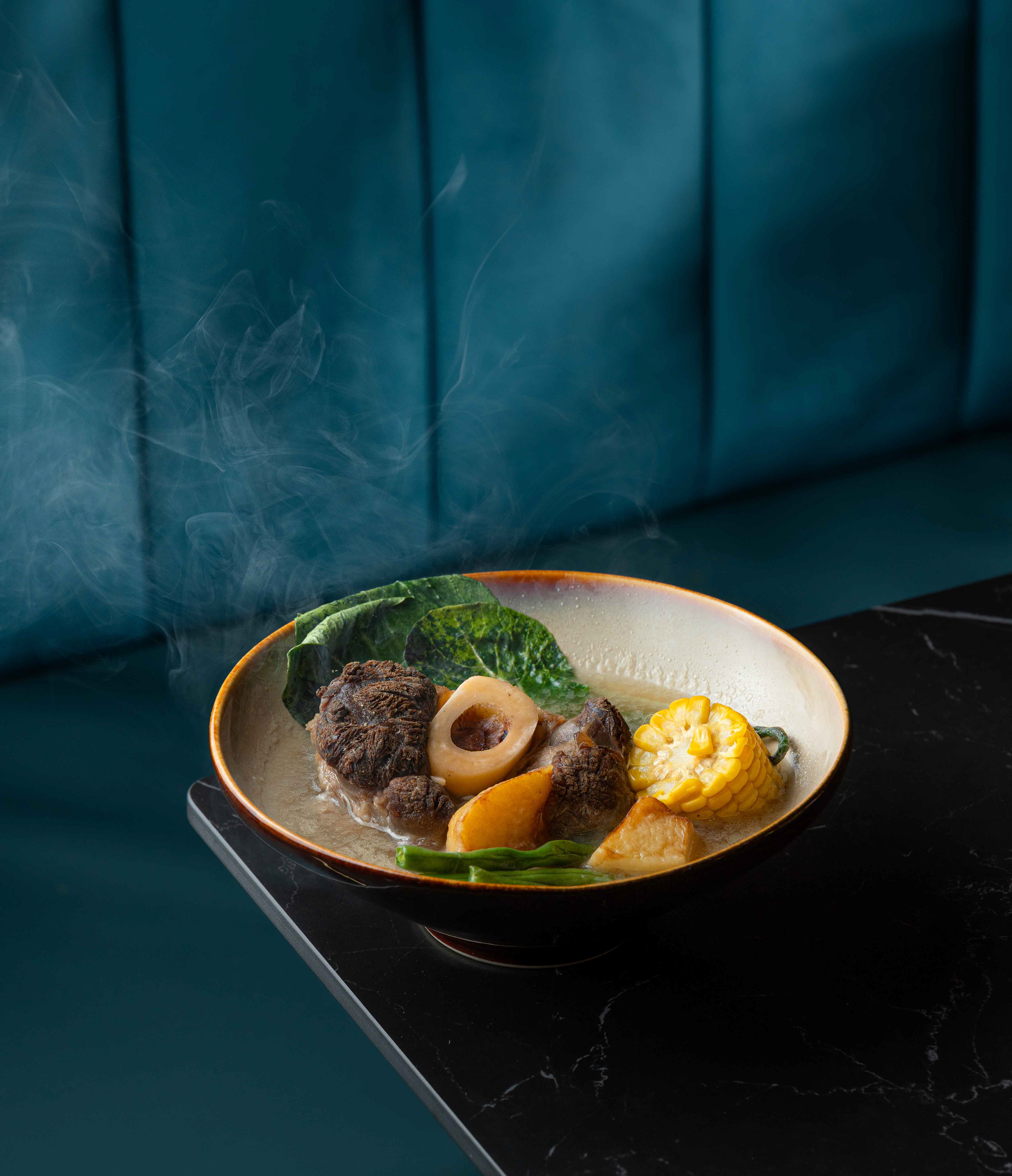 Cinematic food photography of steaming hot bone marrow soup with corn and greens, highlighting professional culinary motion styling and moody lighting for commercial restaurant branding across Canada.