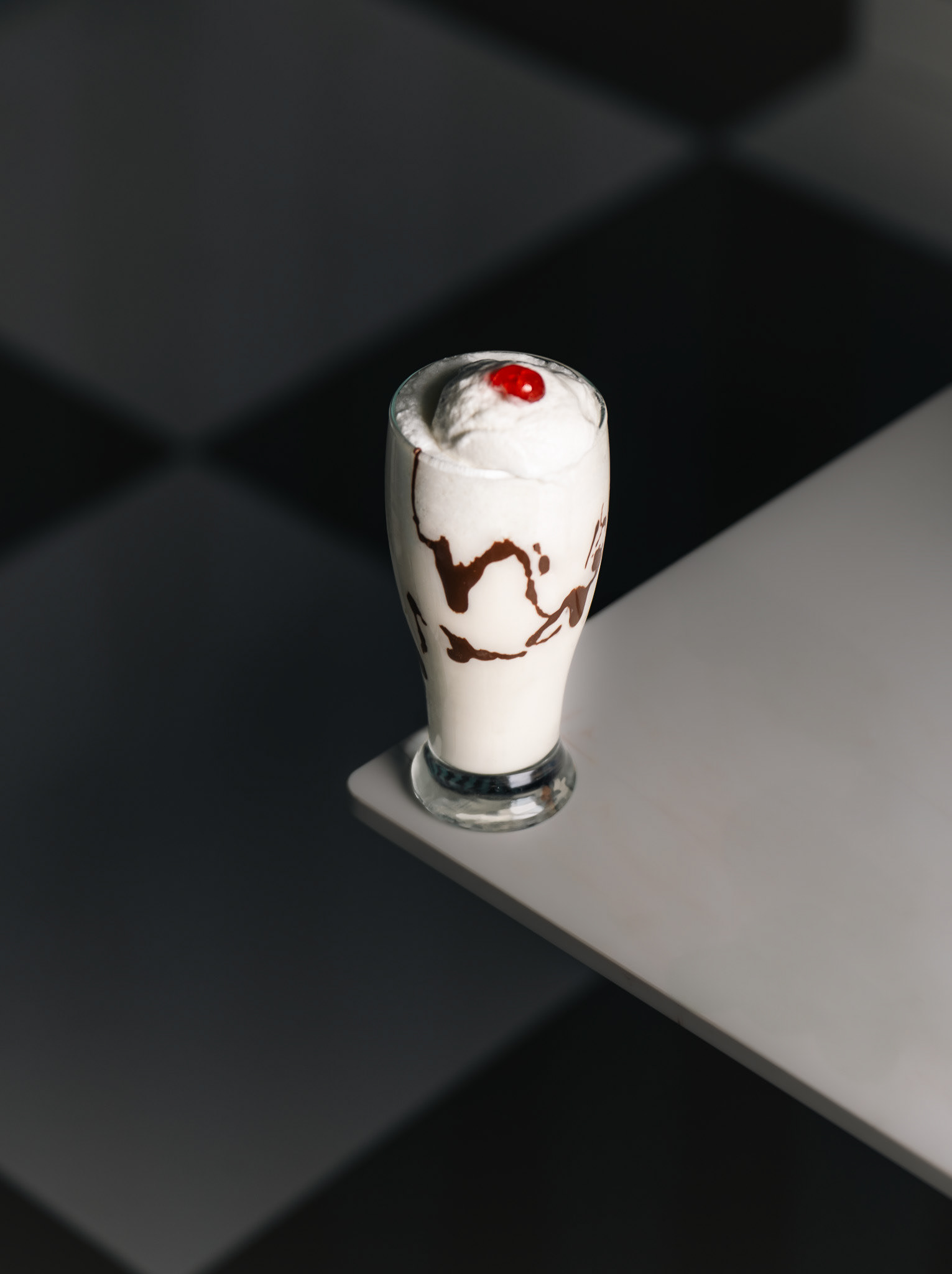 Elegant vanilla milkshake with chocolate syrup drizzle and a cherry on top, minimalist studio food photography for clean social media branding and restaurant menu design in the GTA.