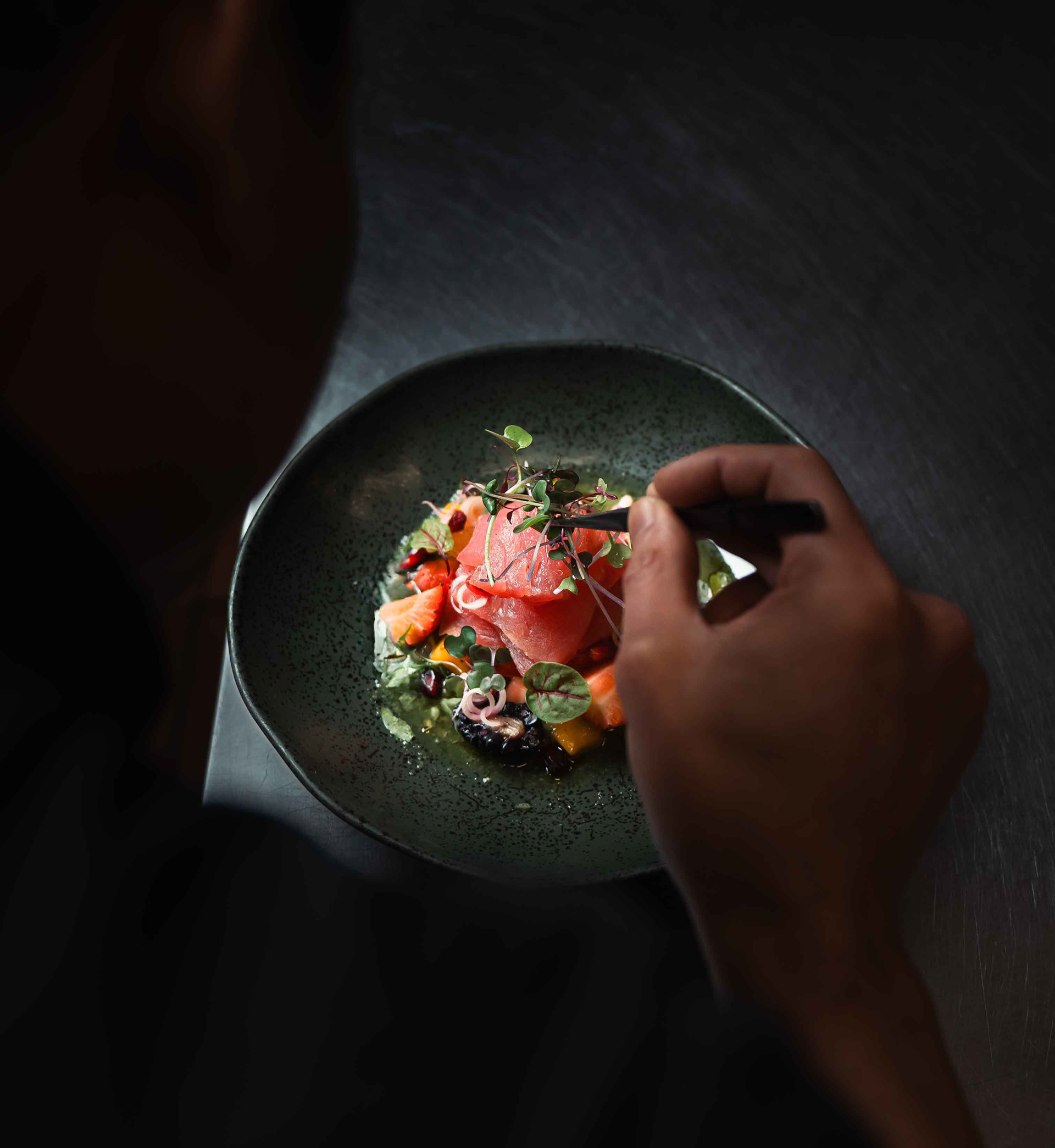 Close-up of a chef’s hand using tweezers for precision plating of a fine dining tuna crudo, editorial food photography capturing the professional process for high-end Toronto restaurant branding.
