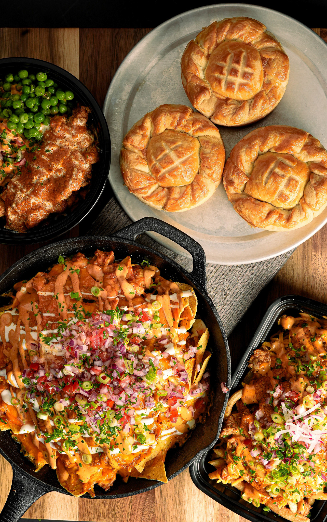 Professional flat lay photography of golden savory pies and loaded nachos in a cast iron skillet, commercial food imagery for Toronto pubs and catering companies specializing in comfort food.