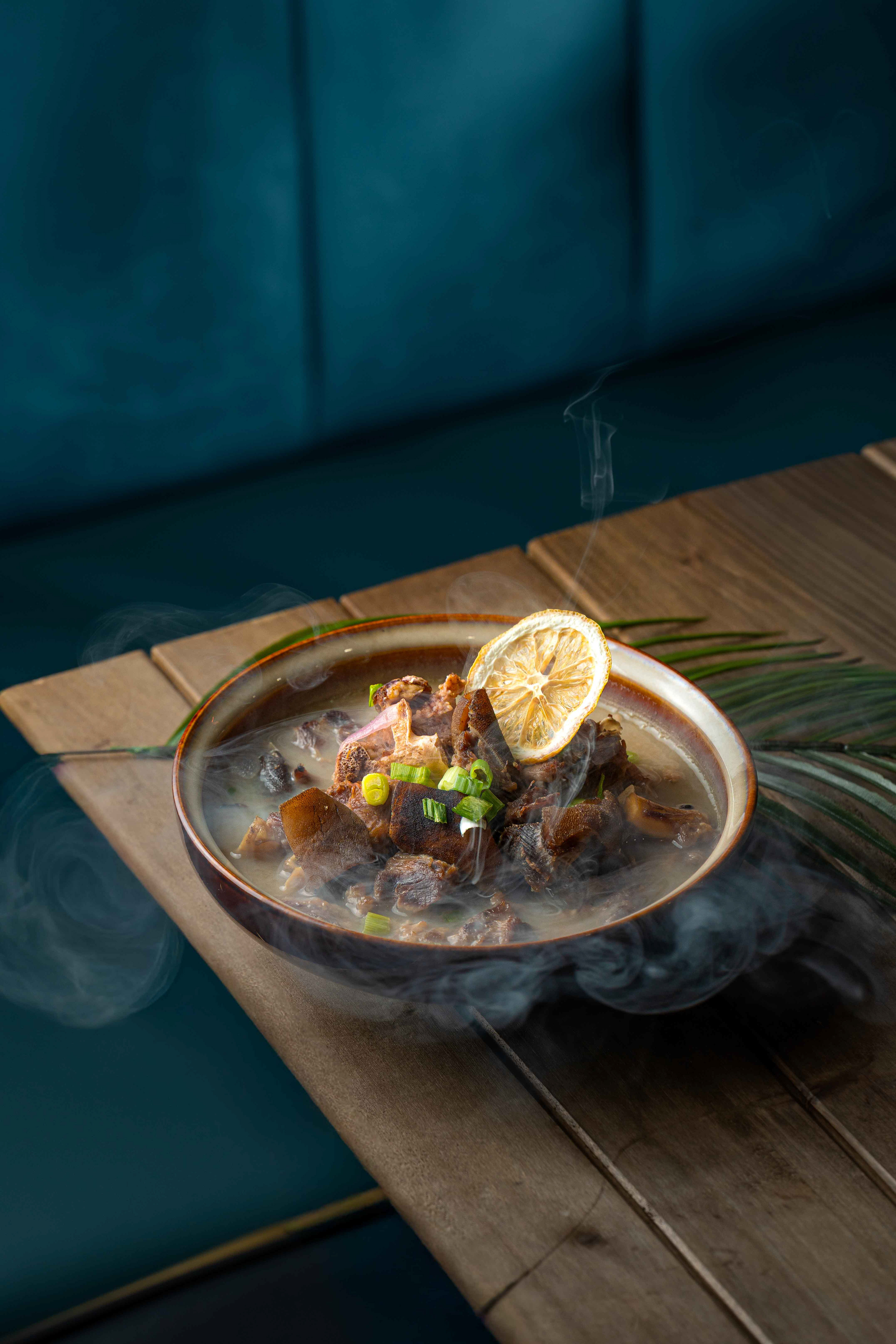 Close-up of a steaming hot gourmet beef stew with a dried lemon garnish on a rustic wooden table, high-quality culinary photography for restaurant menus in the GTA and across Canada.
