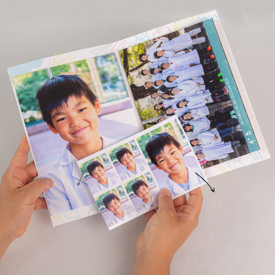 Manos sosteniendo una carpeta escolar abierta con fotos de un niño en guardapolvo: retrato individual, foto grupal del grado y fotos carnet.
