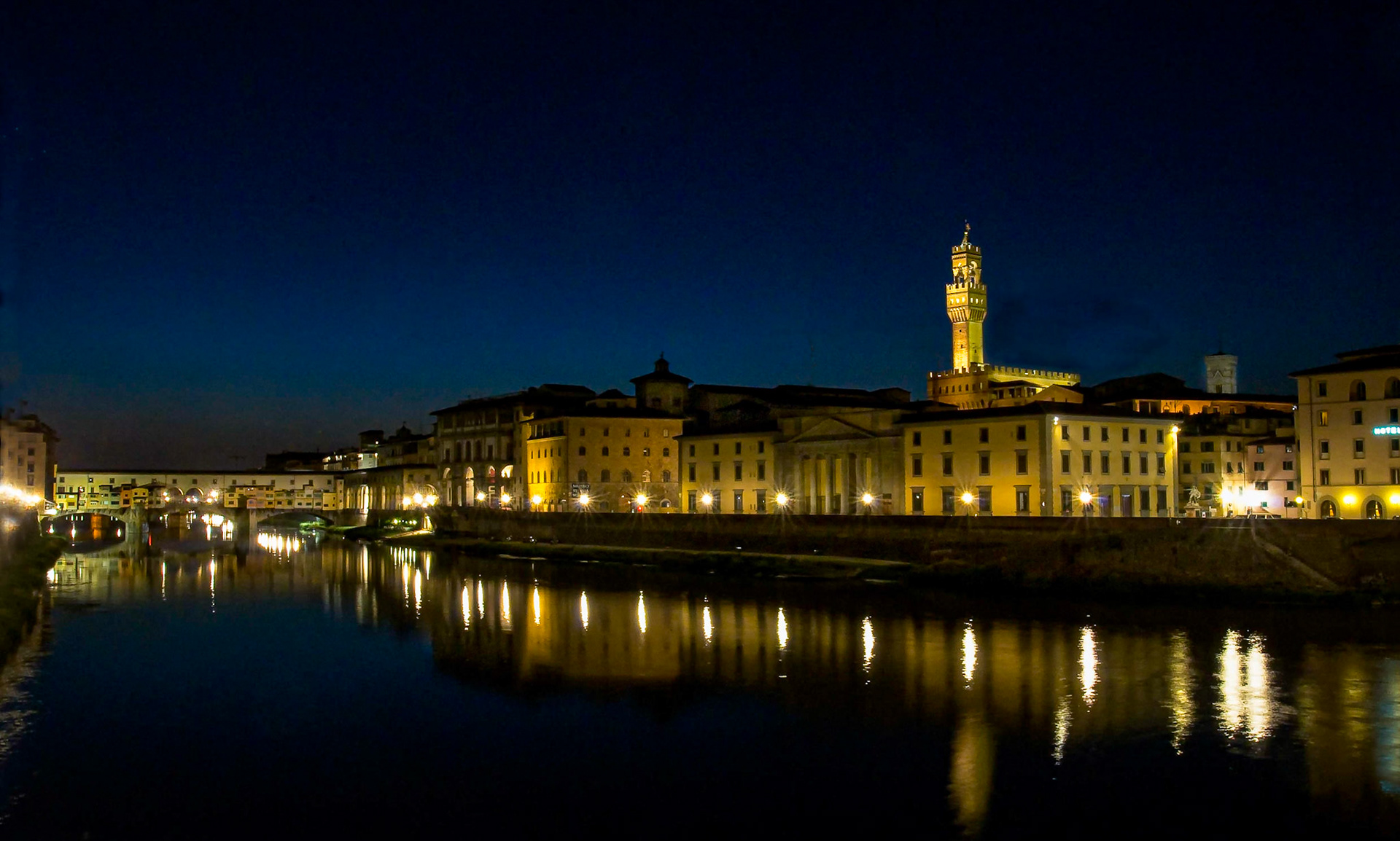 Night settles over the Arno River in central Florence, with the well-illuminated commerce arts buildings as well as the tower of the Palazzo Vecchio reflect3d in the calm water. June 2009