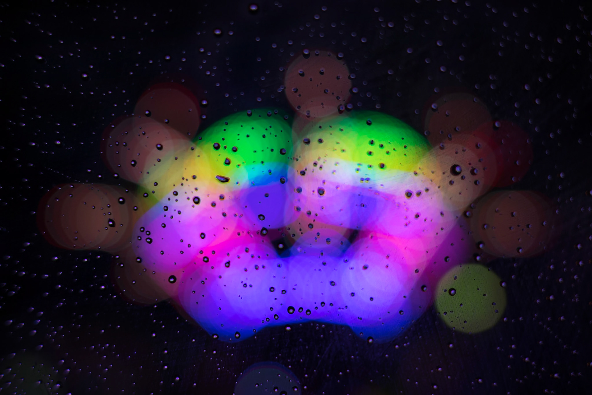 Drops of water dot the window with the carnival lights shining through it.