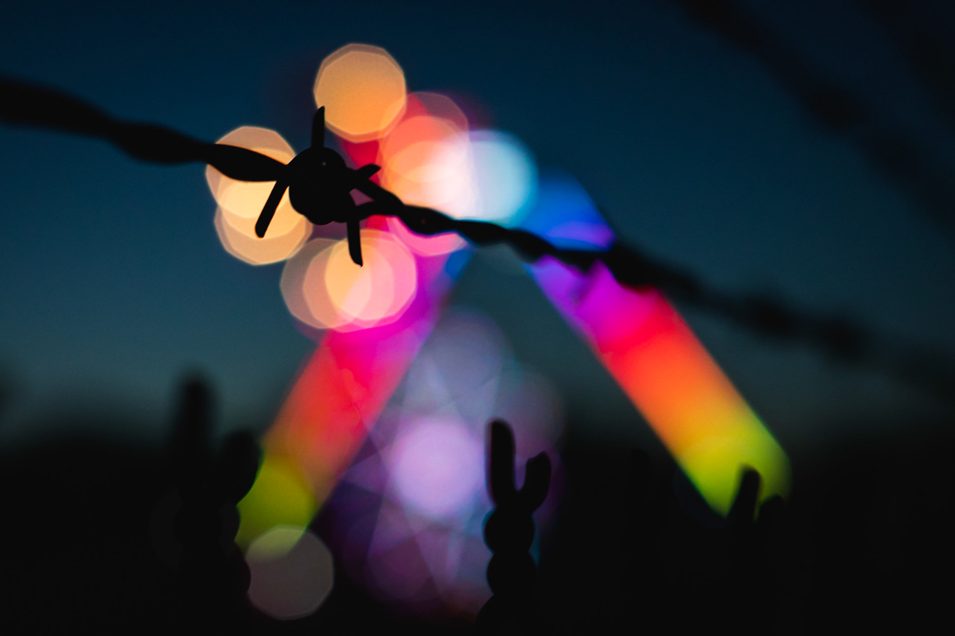 The lights of the carnival shot through a barbed-wire fence.