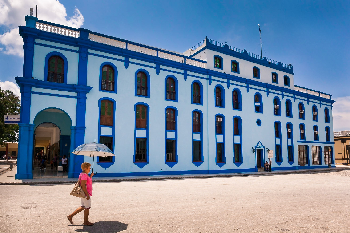 The colored Post Office building of Bayamo with a lady that shelters from the sun under an umbrella, Bayamo, Cuba