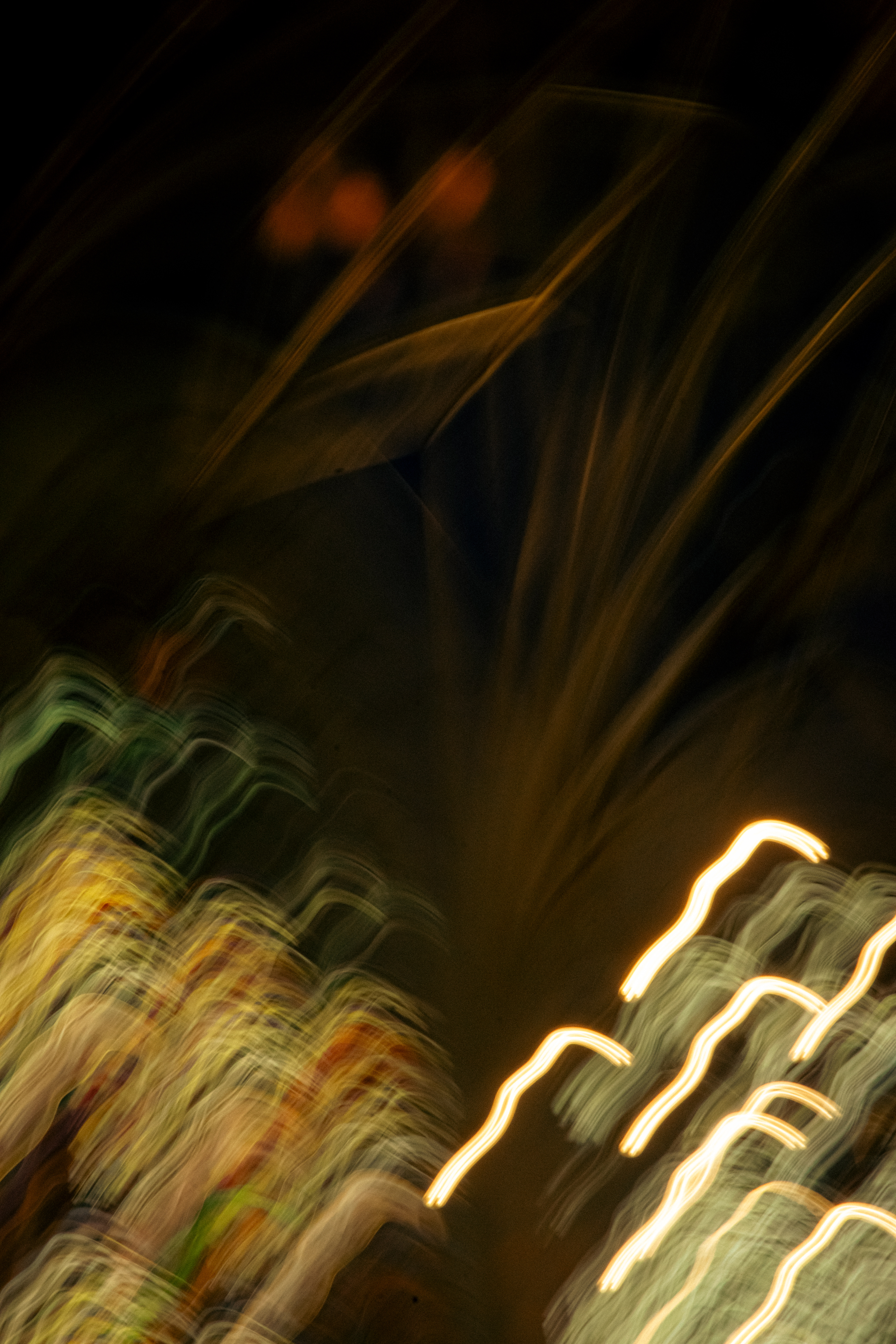 'Earthy Velvet haze' (2025) Waves of colour and light stretch diagonally across a dim, shadowy background. In the lower left and middle, lively streaks swirl in hues of yellow, gold, green, and orange, merging together like paint brushes dragged quickly over a dark canvas. These bright patches look layered and veined, sometimes with spots of reddish brown and hints of purple, adding warmth and depth.     On the right, luminous white and pale yellow zigzag lines arc upwards, creating scribbled textures that pop against the darkness. These lines seem electric and dynamic, as if caught in motion, and their shapes are irregular with uneven curves. In the upper part, the scene is draped in deep shadow, but soft amber and reddish glows peek through faintly, adding a mysterious atmosphere.     Overall, the image’s texture is smooth and flowing, with the colours bleeding and blurring into each other, giving it an impressionistic, almost liquid feel, vibrant at the bottom and calmer at the top.