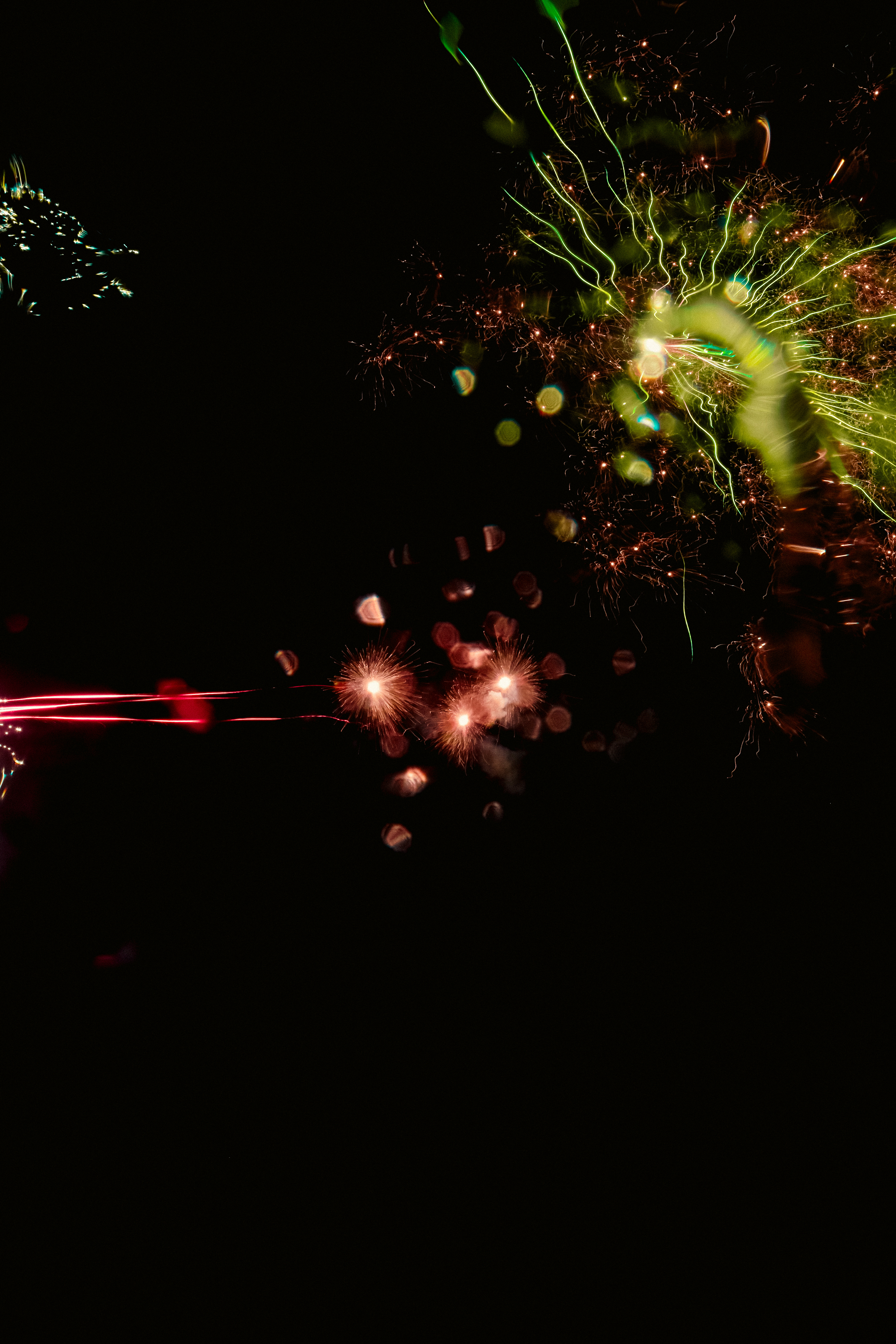 Sparks + Confetti III (2025) Swirling, energetic lines and bursts of color set against an inky blackness. The image features streaks of neon green and electric yellow radiating outward in jagged, tentacle-like patterns from the upper right, with tangled, almost chaotic motion. Small, soft, glowing orbs in orange and red hues cluster and float near the center, appearing like suspended embers or sparks, giving a diffused, dreamy texture. Sharp, bright streaks in magenta and crimson shoot horizontally from the left, slicing through the darkness and leaving delicate trails behind. The composition feels dynamic and lively, with elements evoking both the sharp crackle of energy and the gentle haze of smoke or mist, creating a blend of sharp lines and soft, bokeh-like textures amid the void.