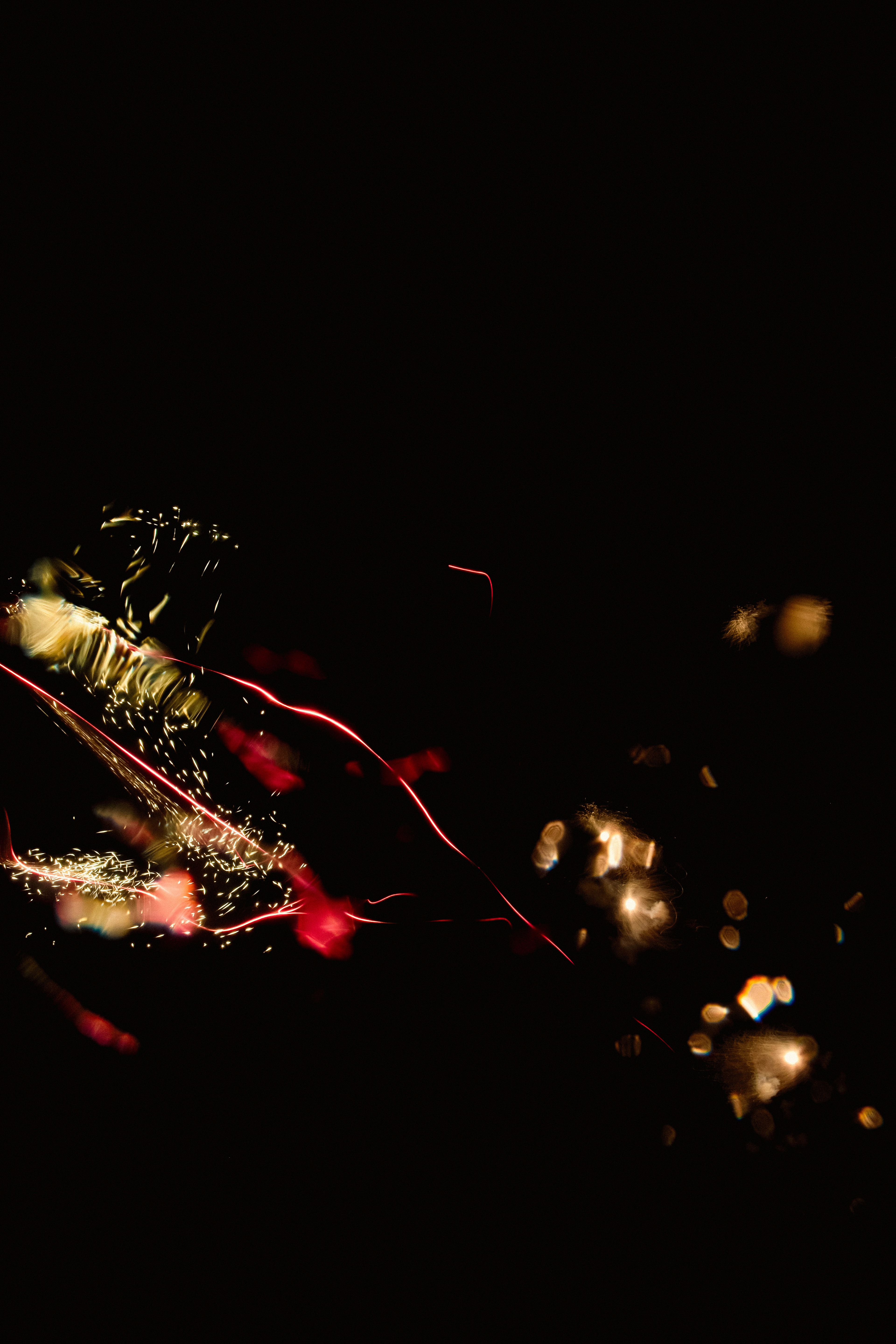 Sparks + Confetti II (2025) Glowing fragments and vibrant, swirling streaks of light set against a deep black background. Fine threads of red light twist and sweep across the lower half, with bursts of gold and white sparkling like tiny embers or firework trails. There are clusters of bright, honey-colored bokeh dots and soft, fuzzy flares, giving the image a sense of depth and energy. The textures vary from needle-thin lines to hazy, glowing patches, creating a lively, almost electric feel. Touches of subtle green and peach blend with the reds and yellows, adding to the overall richness and complexity of the visual display.