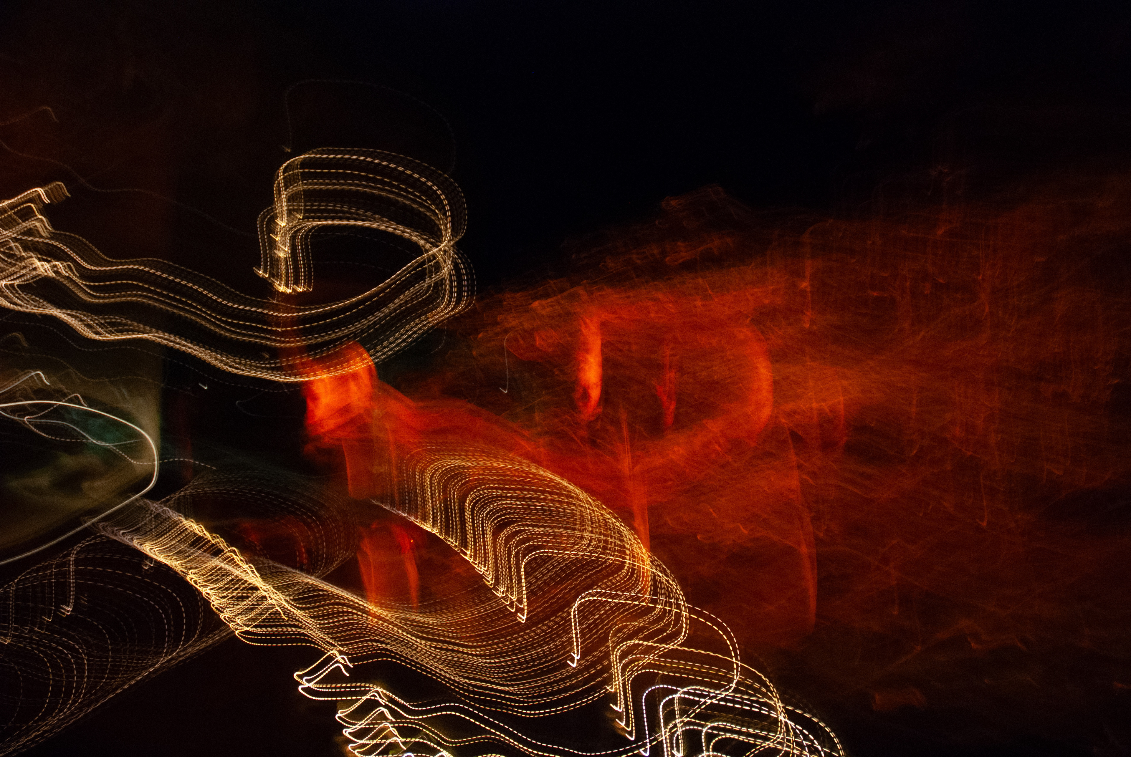 'Human Light Clone Four Face' (2018). A synthesis of light and colour unfolds against the canvas of night. Fiery orange hues swirl like ethereal flames, casting a warm glow that seems to pulse with life. Intertwined with these vibrant embers are delicate ribbons of white light, weaving intricate patterns that resemble graceful arcs. The scene captures a moment of dynamic energy, where light becomes both artist and muse, painting an abstract masterpiece in the darkness.