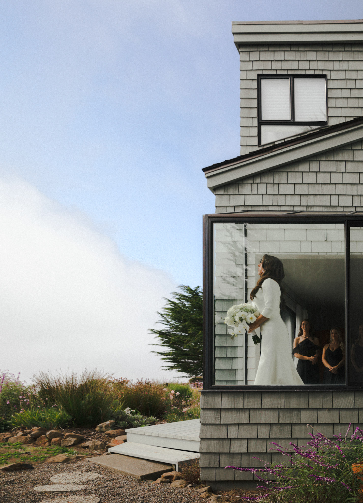 Bride holding a white bouquet pauses in the doorway at Sea Ranch Lodge on the Northern California coast.