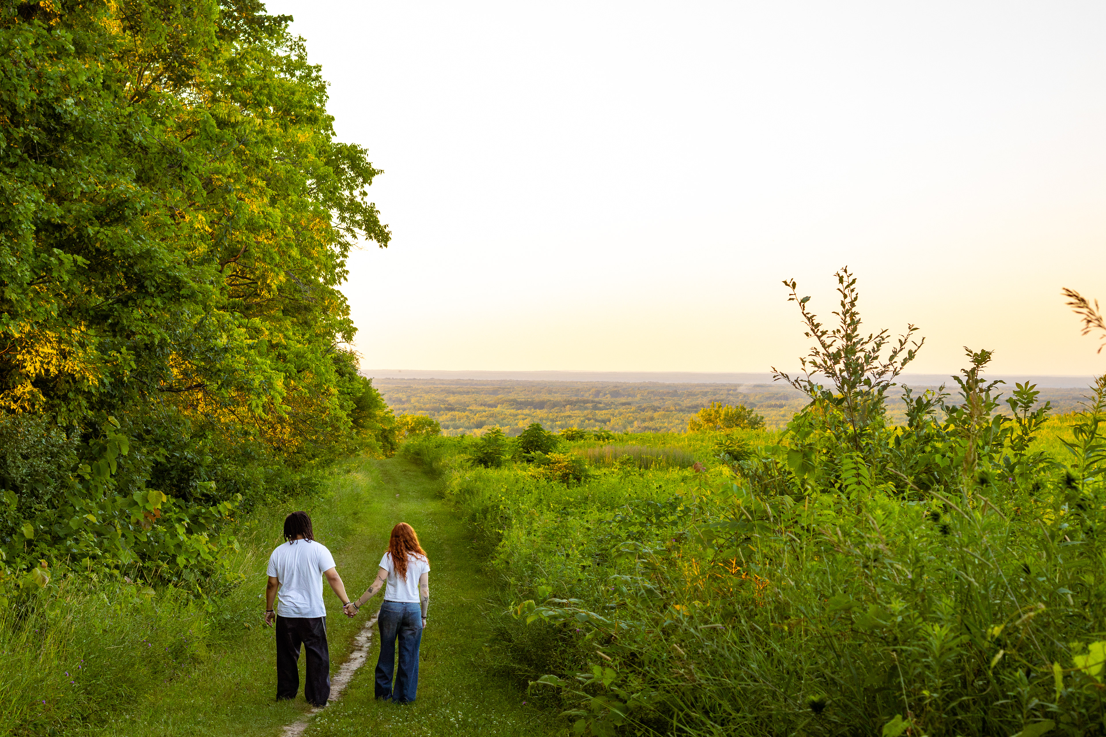Couple walking together through a wooded path overlooking the landscape.