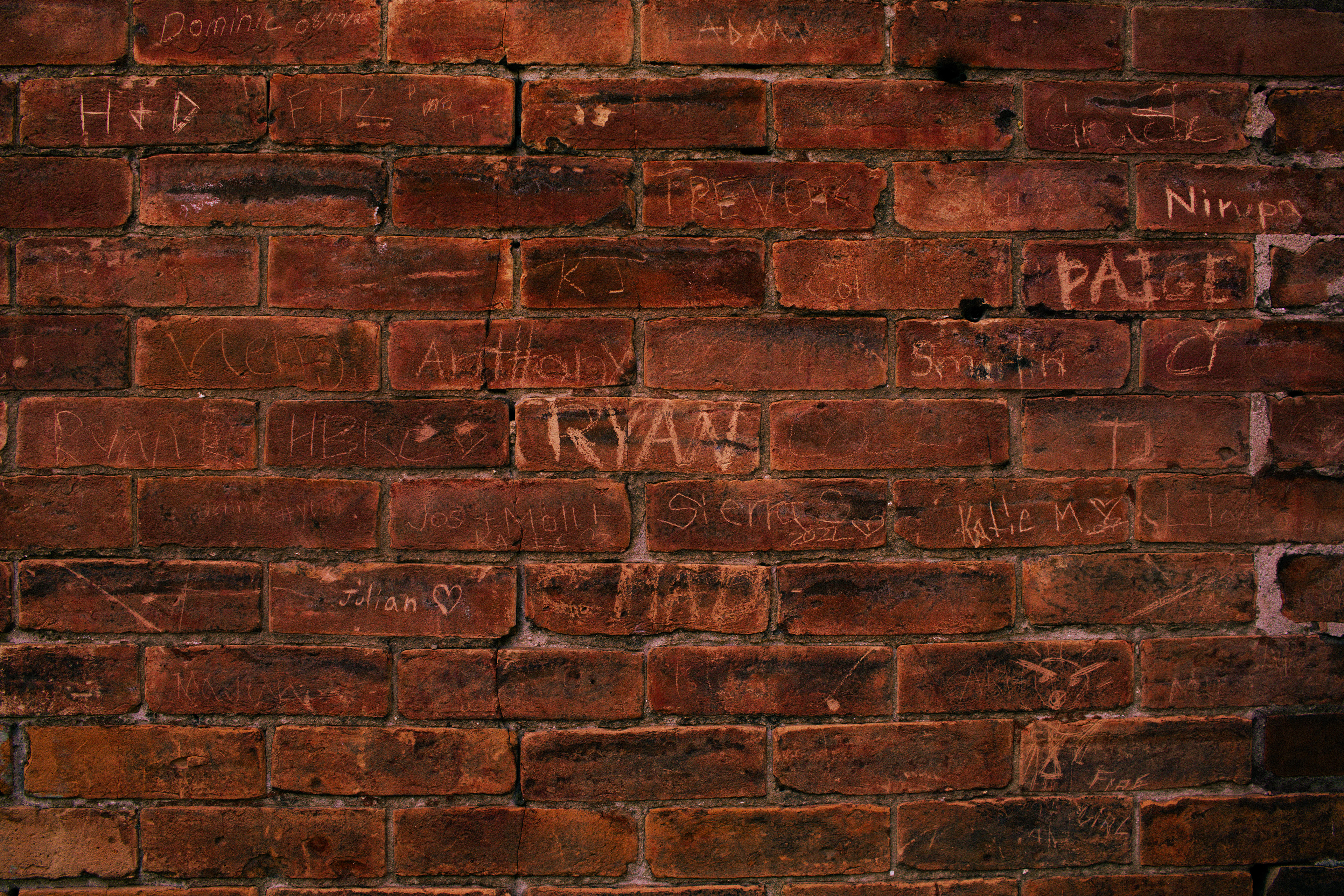 Weathered brick wall covered in layers of handwritten names and markings.