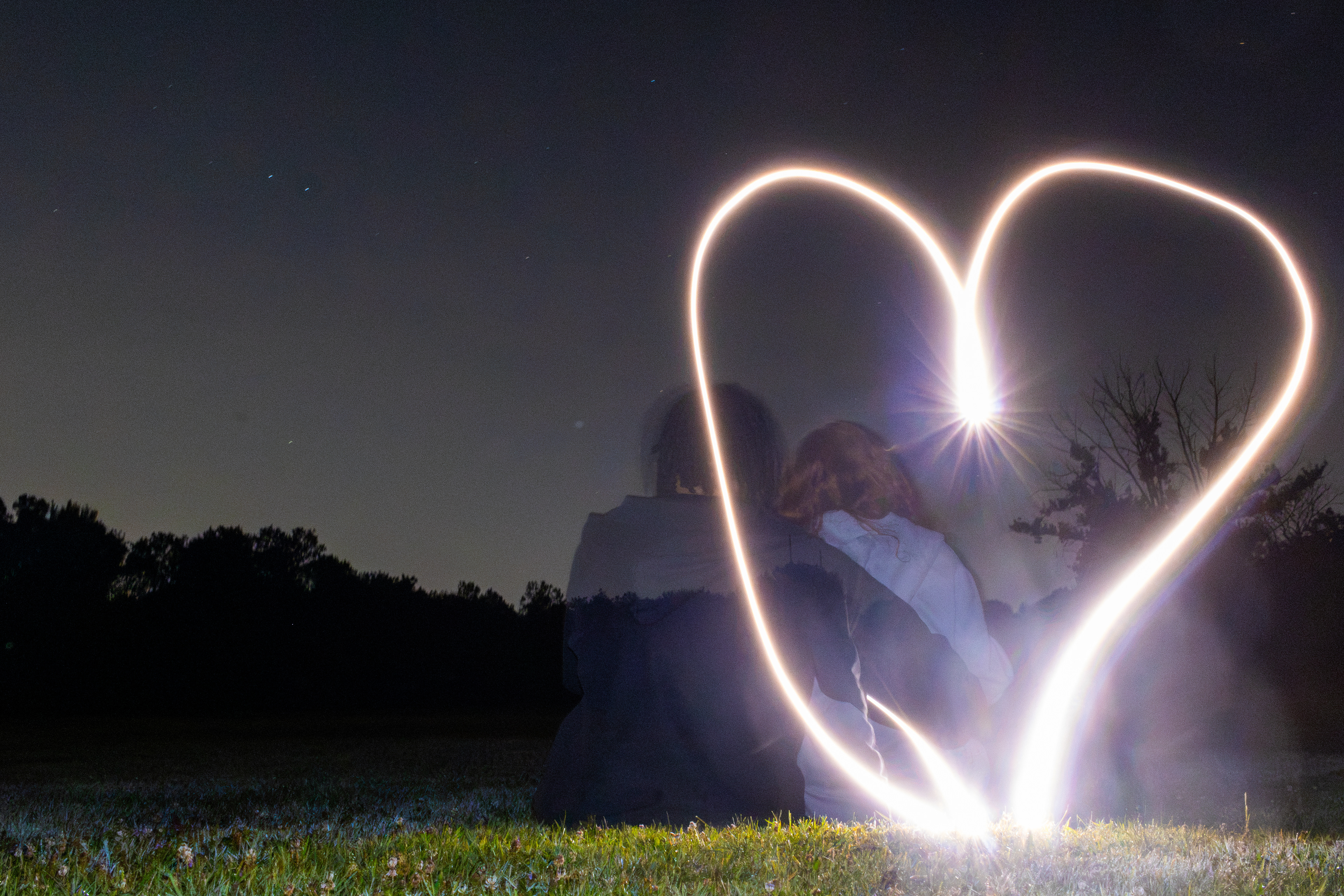 Long-exposure photograph of couple surrounded by a glowing heart-shaped light.