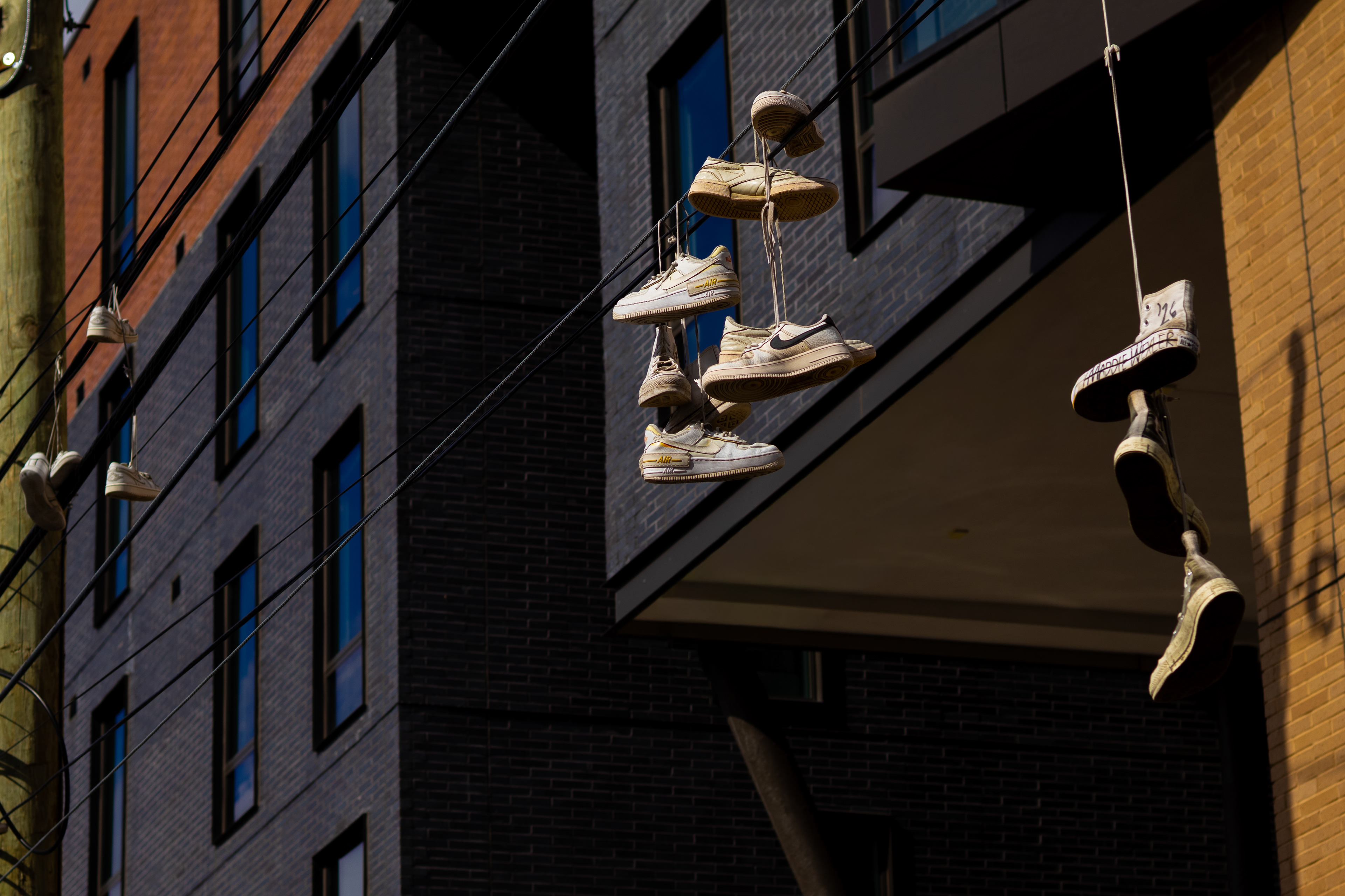 Sneakers suspended from wires along the side of a city building.