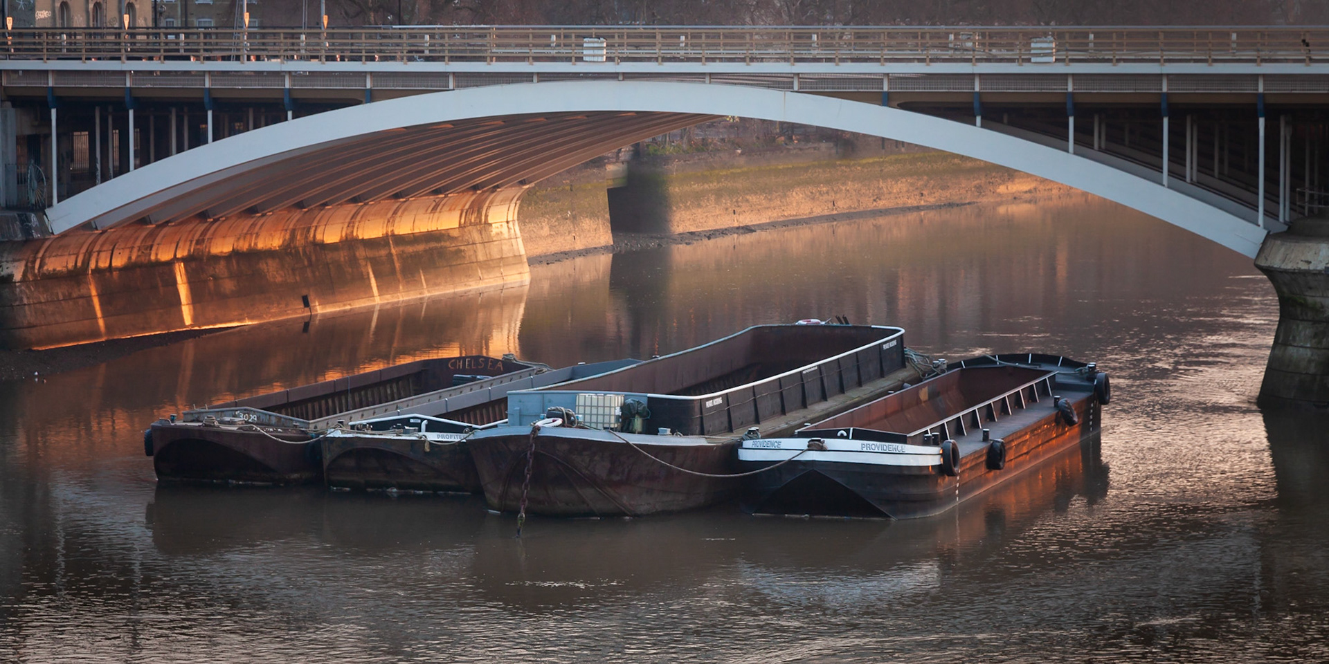 The warm light of a very cold winter morning paints some moored barges and the underside of a bridge, London, England.