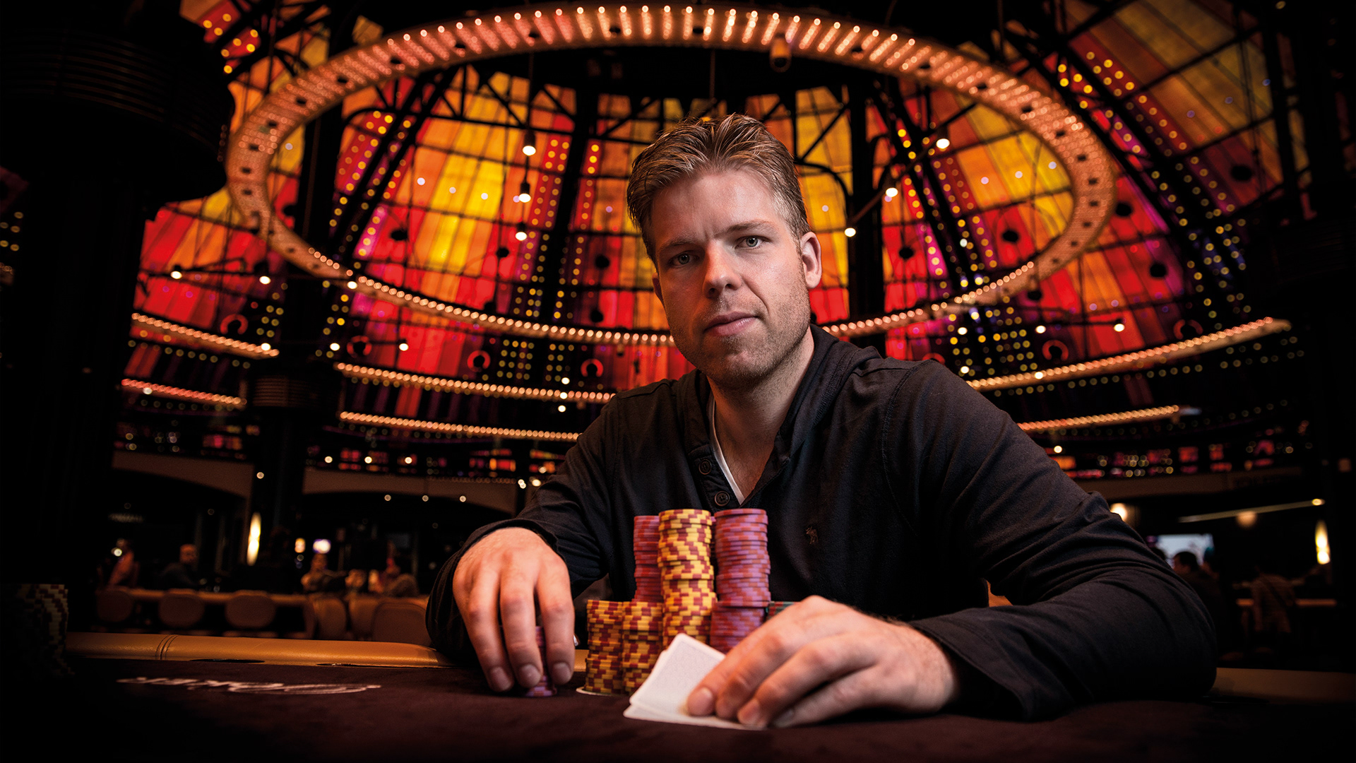 Pokerstar Jorryt van Hoof posing beneath the orange glass dome of Holland Casino Amsterdam with pokercards and fiches..