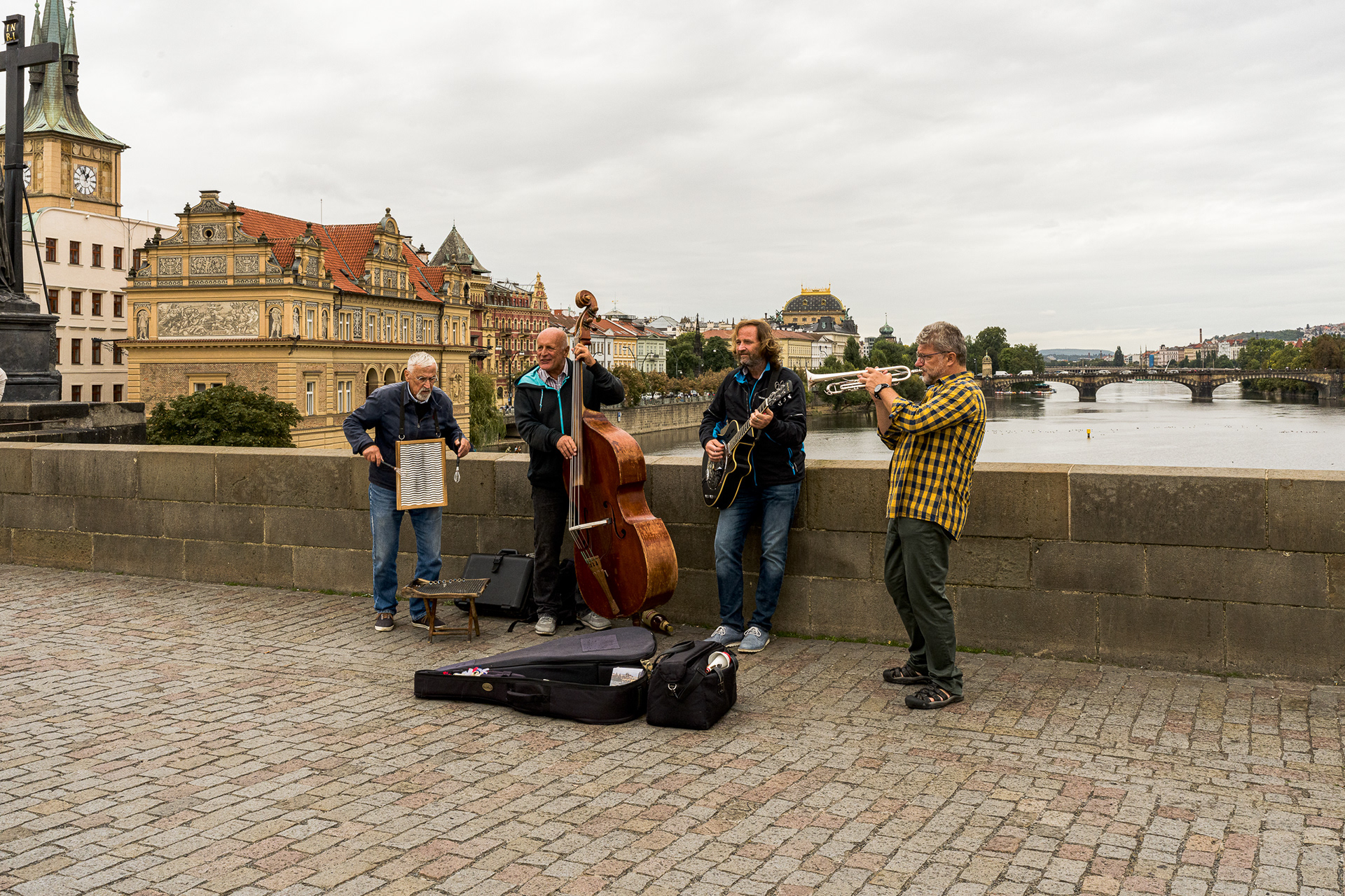 A jazz quartet playing instruments on the Charles Bridge in Prague with the city skyline in the background.