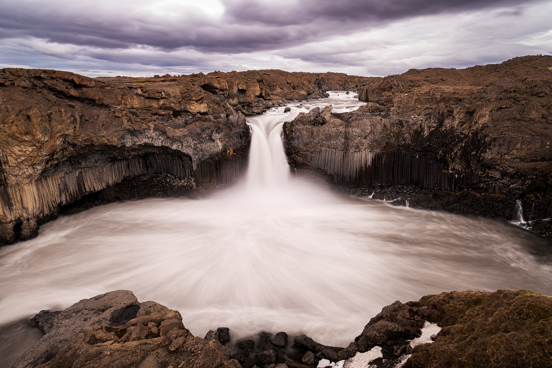 Dramatic long exposure of Aldeyjarfoss waterfall in North Iceland, featuring powerful white water framed by symmetrical dark basalt stone columns.