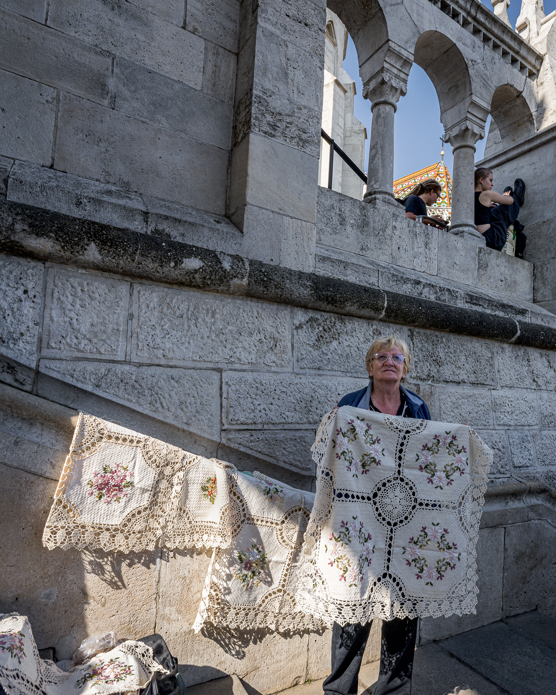 An elderly woman selling traditional handmade white lace on a stone stairway at Fisherman's Bastion.