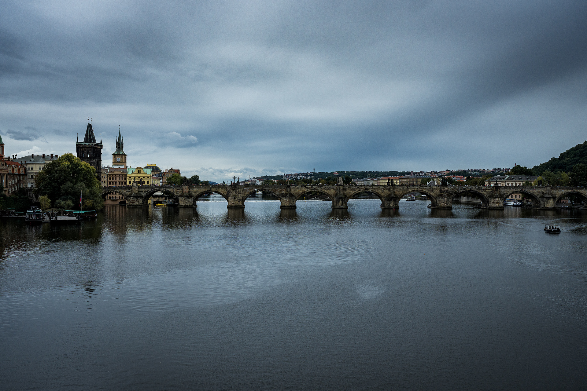 Panoramic view of the Charles Bridge in Prague spanning the Vltava River on a moody overcast day.