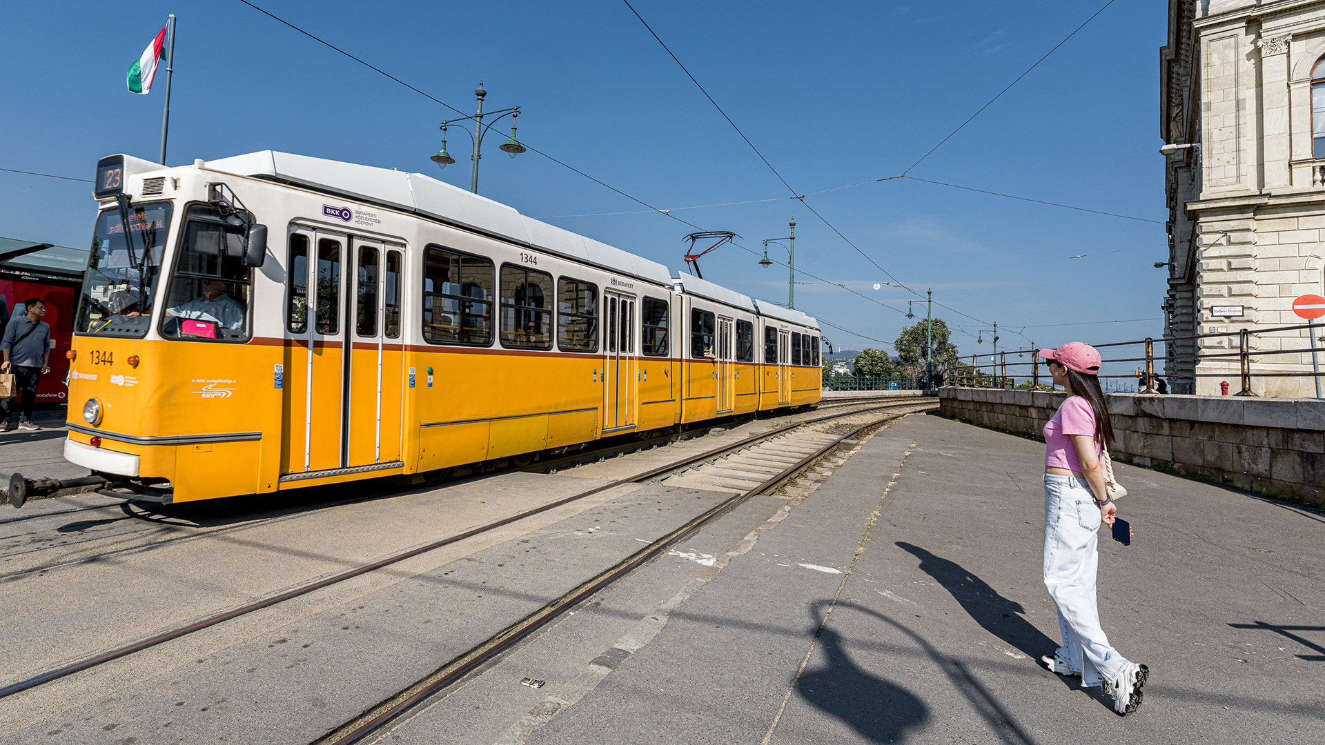 The iconic yellow tram of Budapest passing along the Danube bank under a bright blue sky.