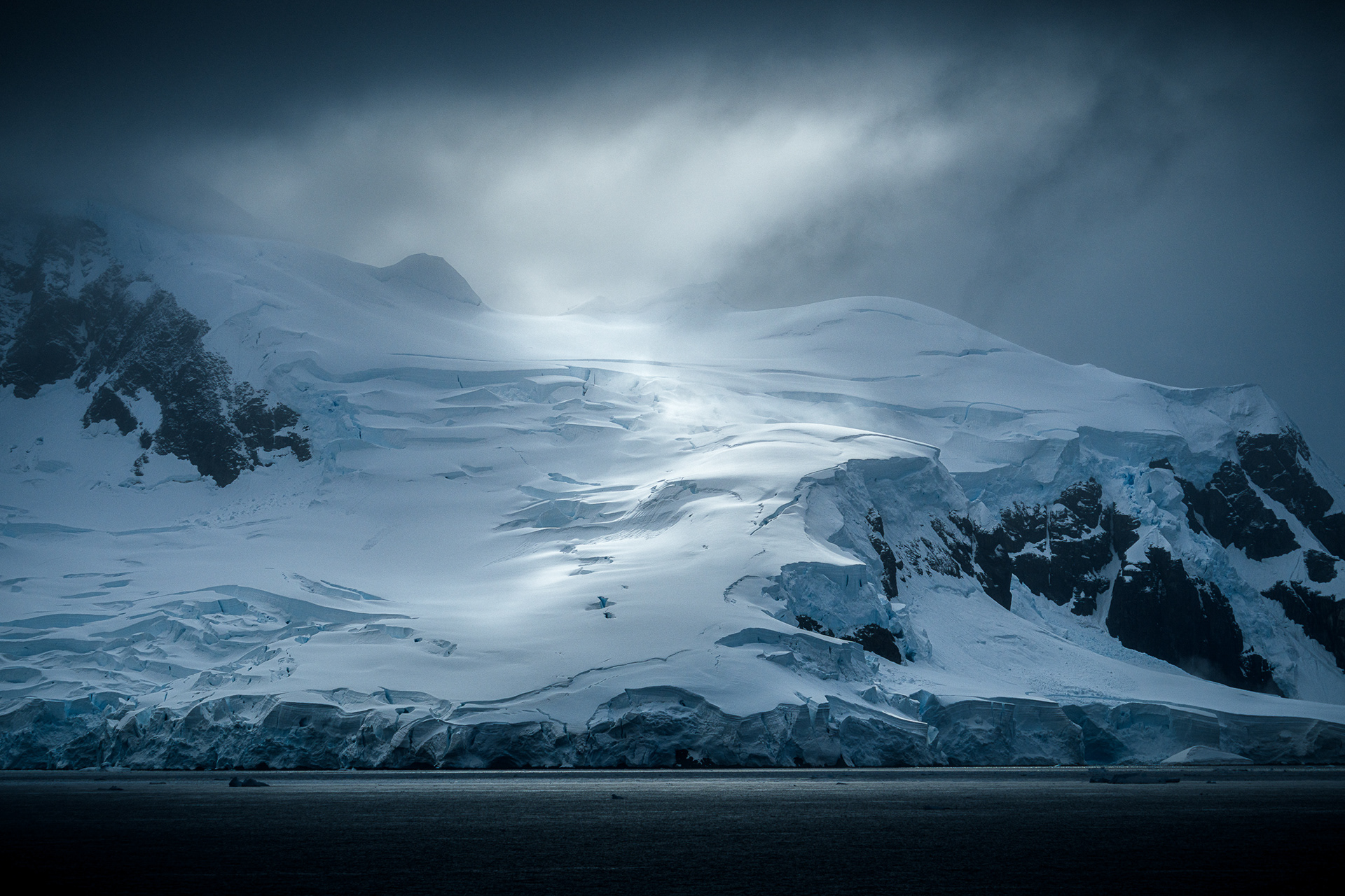 A sun-struck glacier mountain peak in the Antarctic interior. A fine art landscape study of light and shadow, capturing the isolation, geological silence, and ethereal beauty of the frozen continent.