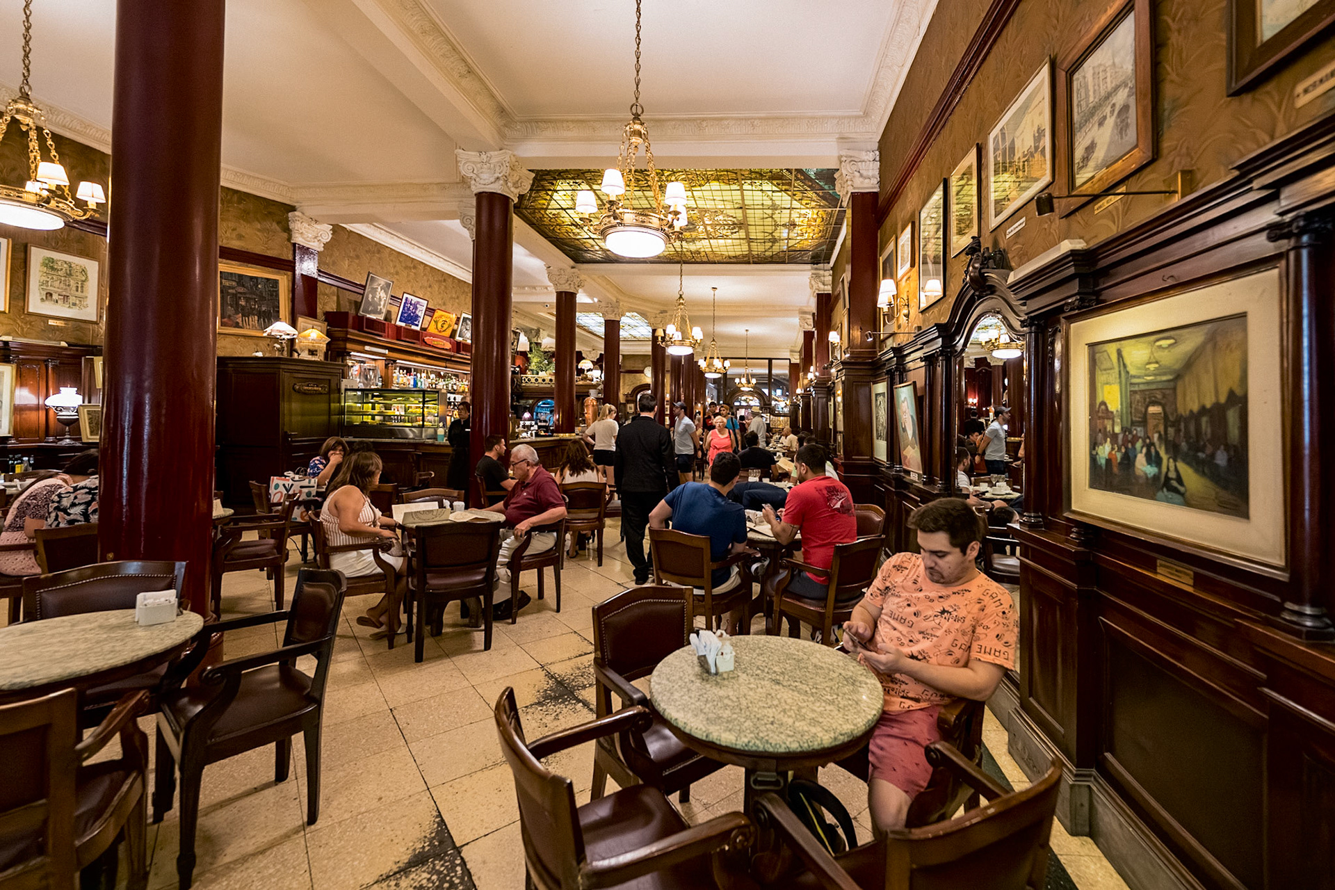 Interior of Café Tortoni in Buenos Aires, filled with people enjoying coffee, surrounded by elegant woodwork, chandeliers, and artwork.