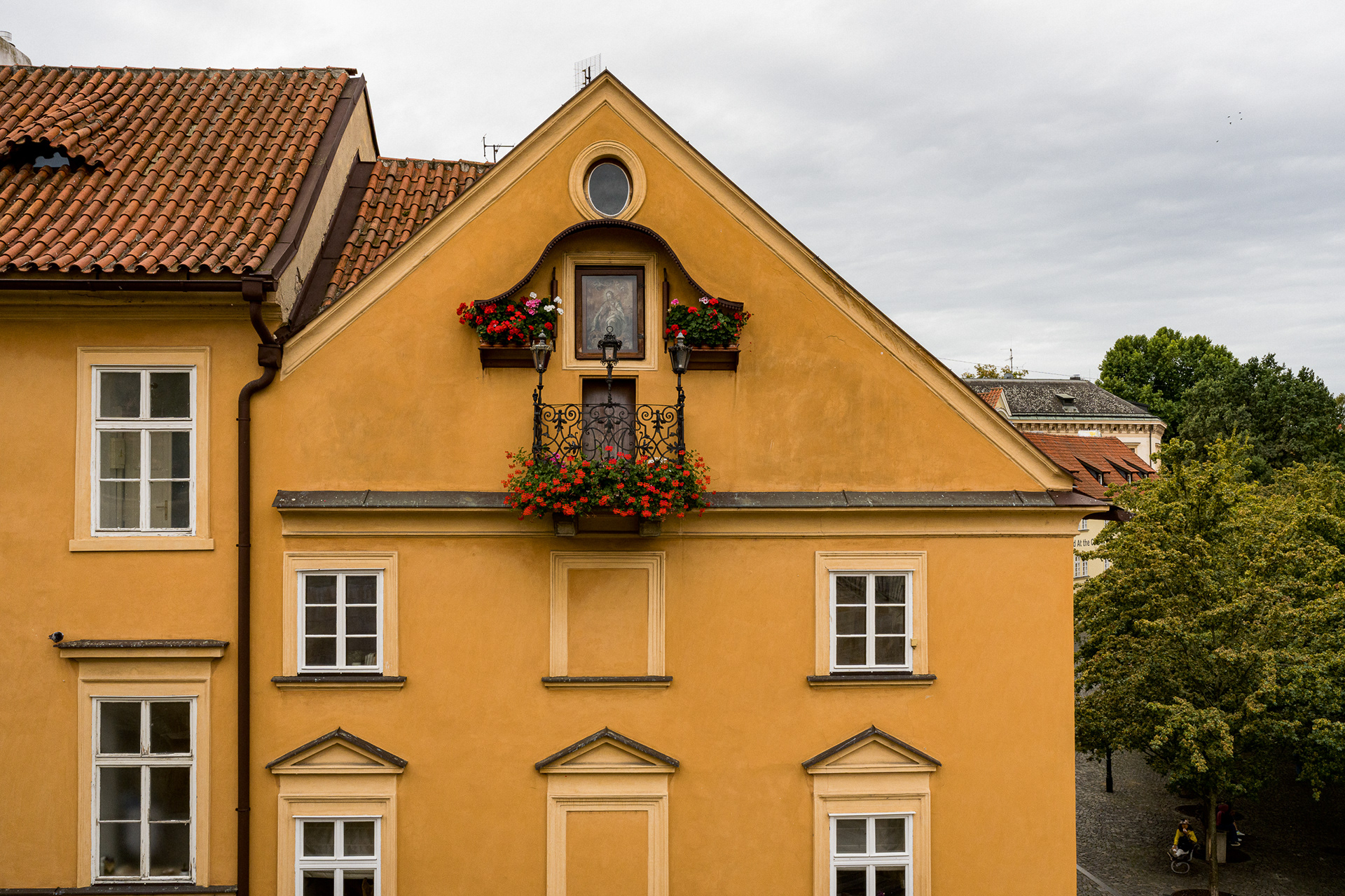 Symmetrical yellow baroque building facade in Prague featuring a wrought iron balcony and red geraniums.
