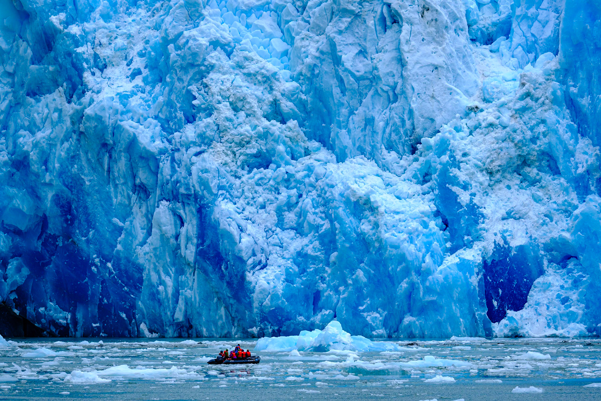 A small inflatable boat carries tourists close to the face of South Sawyer Glacier, Tracy Arm fjord, Alaska.