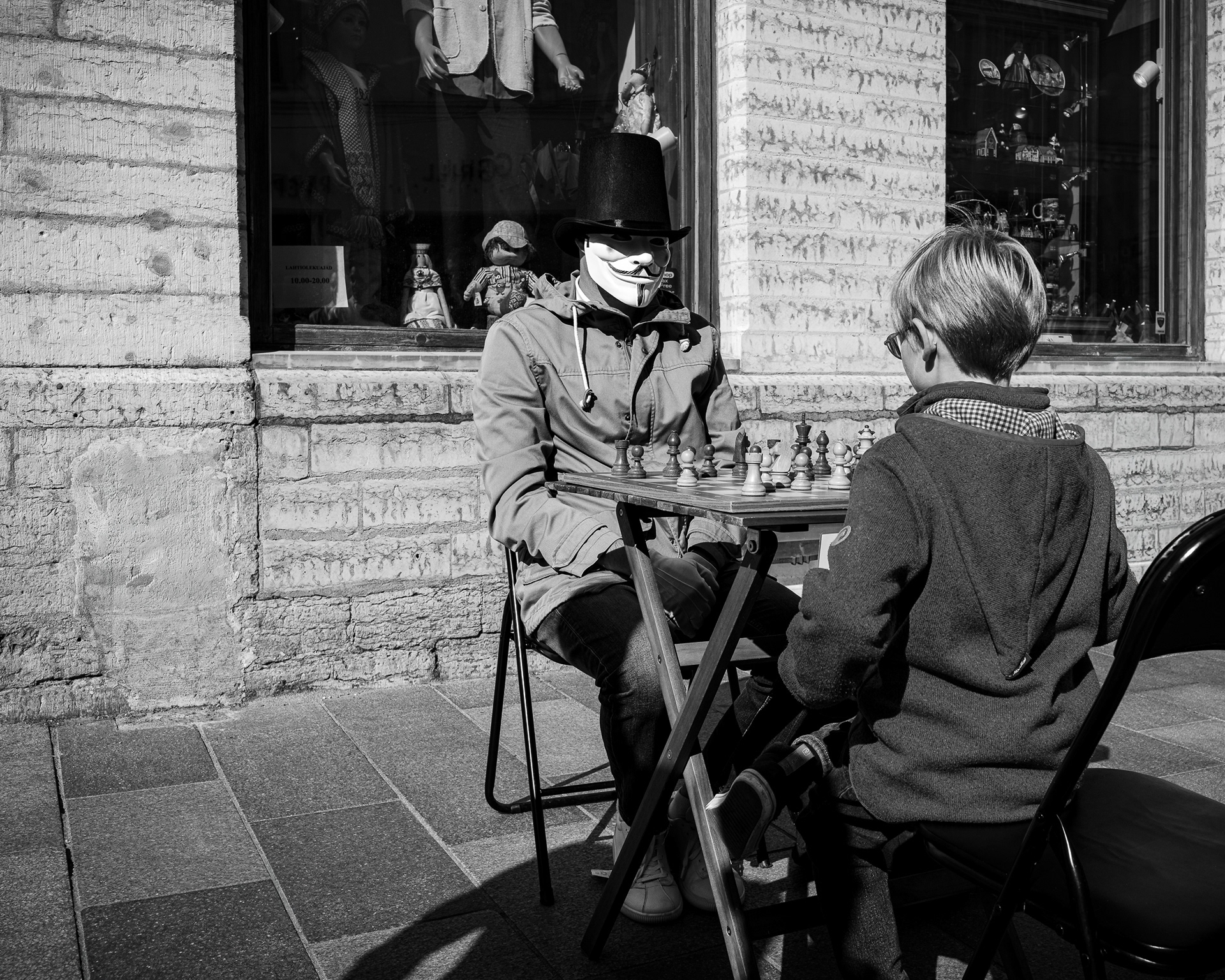 Candid street photography of men playing chess on cobblestones in Tallinn Old Town, Estonia. Muted monochromatic fine art print featuring historic European architecture.