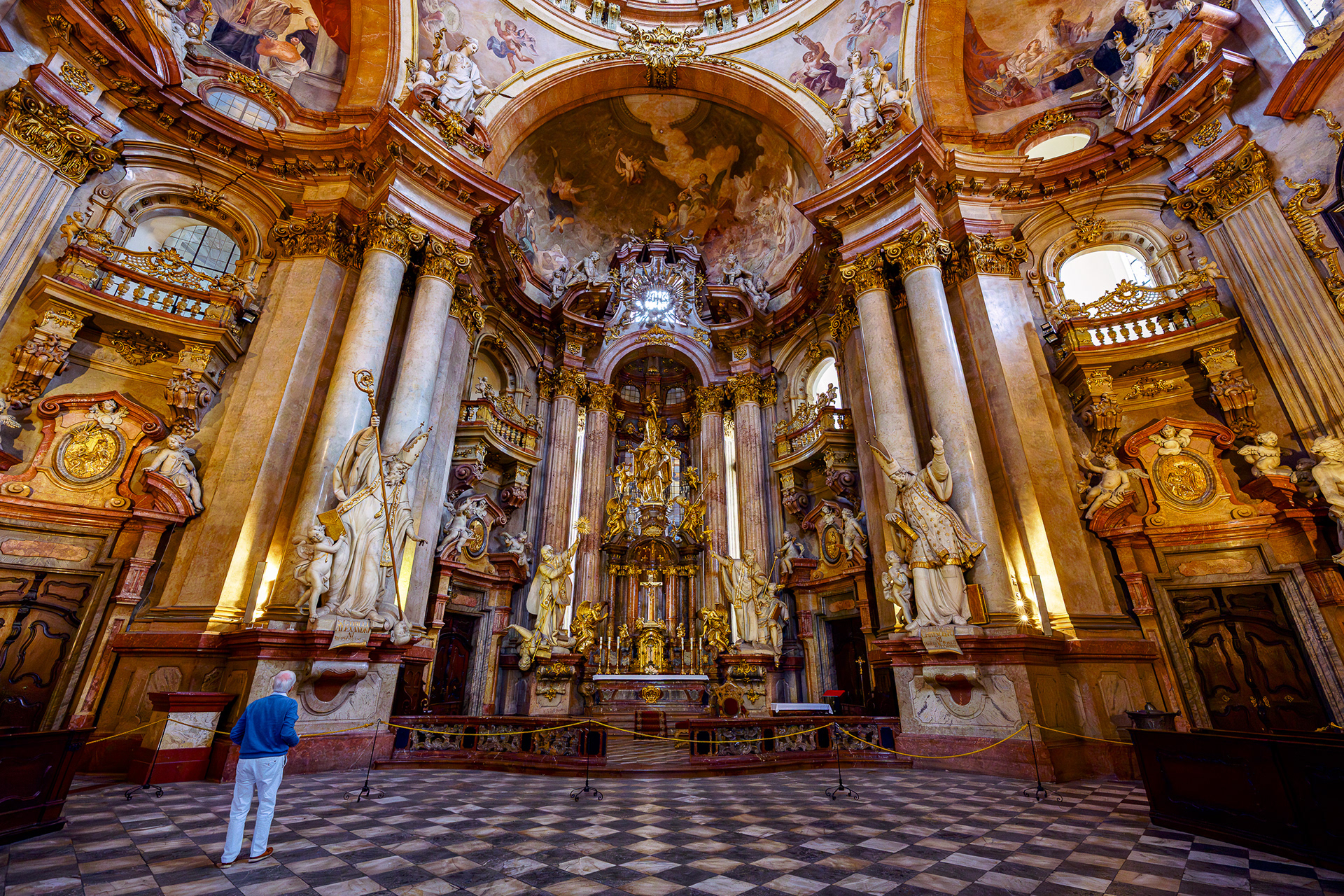 Interior view of a Prague cathedral featuring a black and white checkered floor leading to a gold altar.