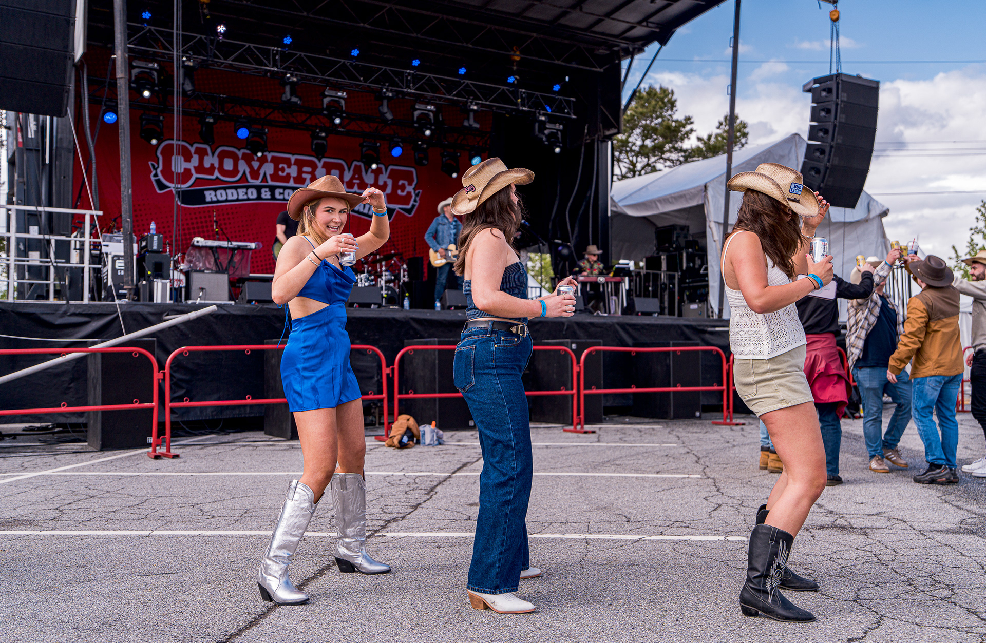 Three women in cowboy hats and western attire dancing and laughing at the Cloverdale Country Fair.