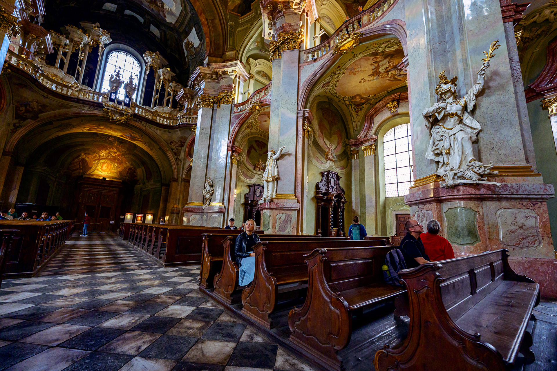 Detail shot of dark wooden pews and a white marble baroque statue inside a Prague church.