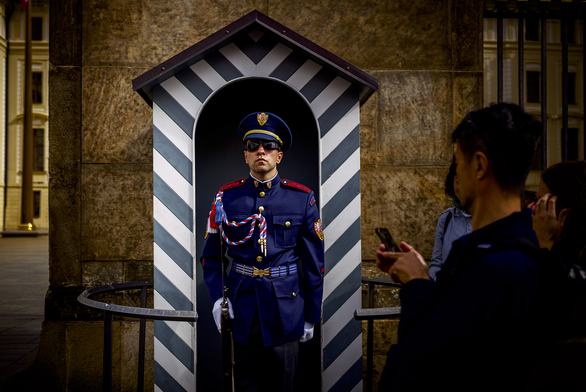 A Prague Castle guard in a blue ceremonial uniform standing stoically in a striped sentry box.
