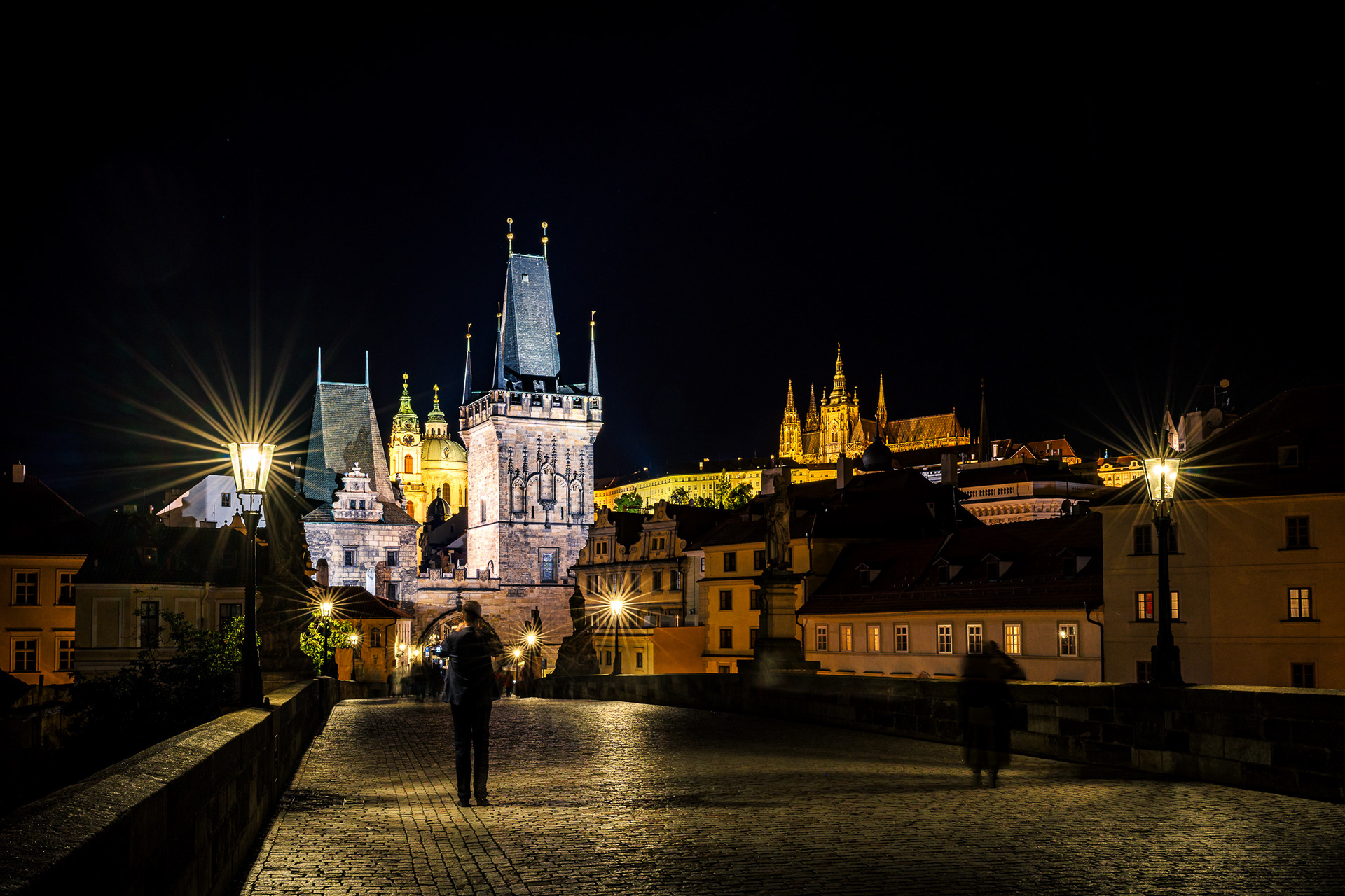 Night long exposure of the Prague Castle and Bridge Tower illuminated by streetlights against a black sky.