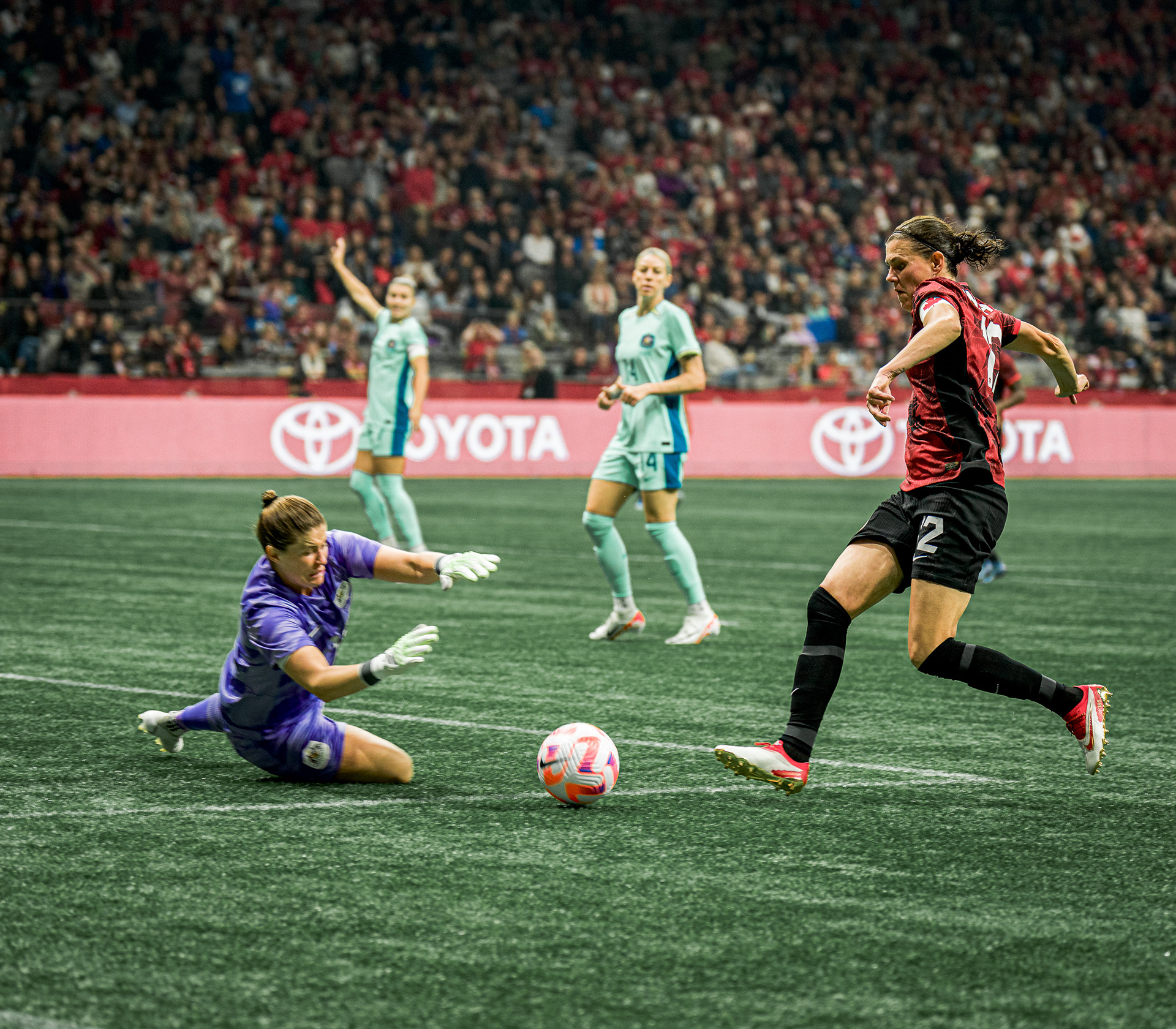 Christine Sinclair challenging the goalkeeper for the ball in the penalty area.
