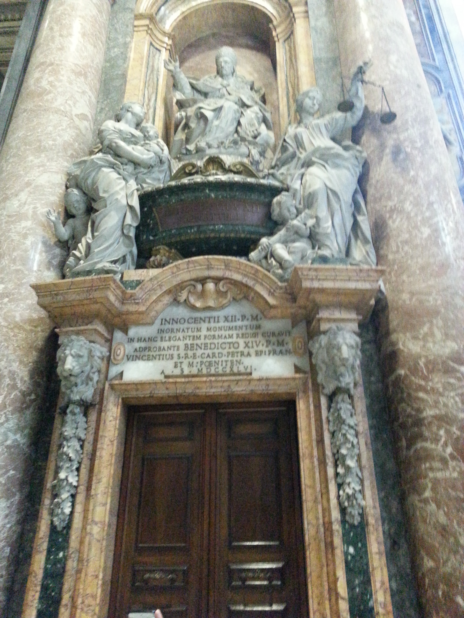 The Monument to Pope Innocent XII (1691-1700) by Filippo Della Valle, has a simple composition - an urn is surmounted by a statue of the Pope, flanked by the allegorical figures of Charity and Justice and crowned at the top by two angels which support the coat of arms - but with a greater height development, due to the restricted space. 